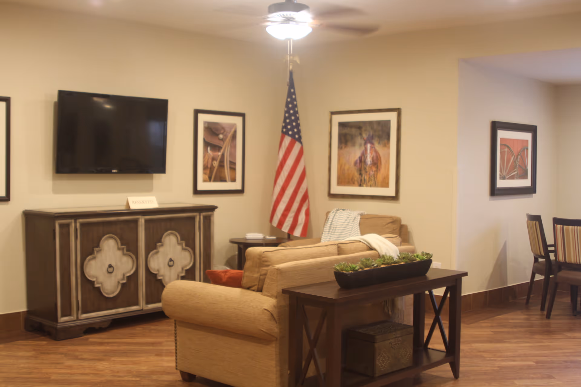 A cozy senior living common area with sofa, coffee table, TV, and American flag.