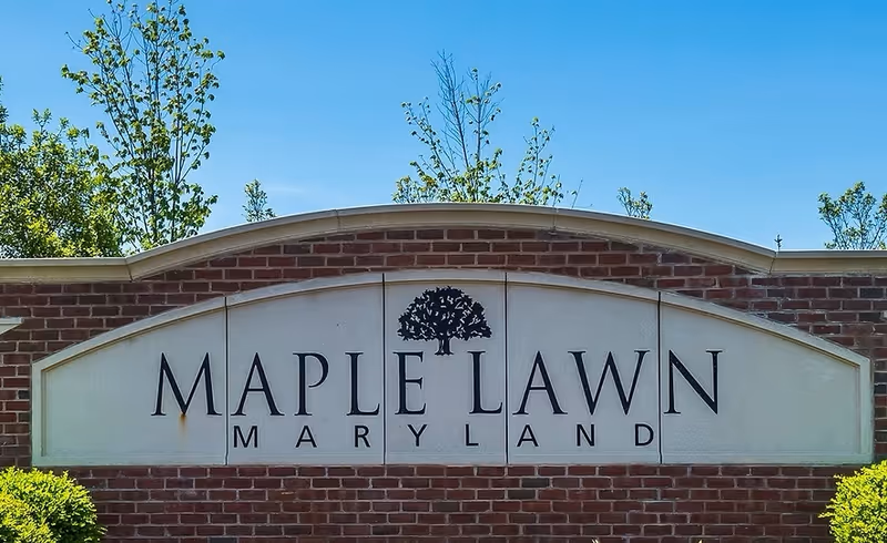 Brick sign reads Maple Lawn Maryland with a tree graphic under a clear blue sky