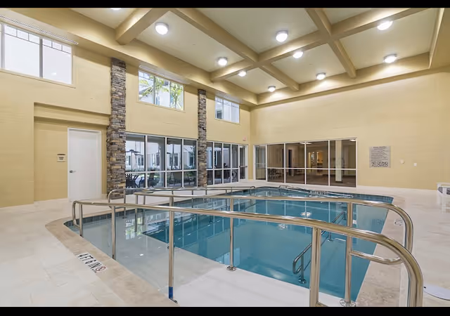 Indoor pool area in a senior living facility with railings and large windows.