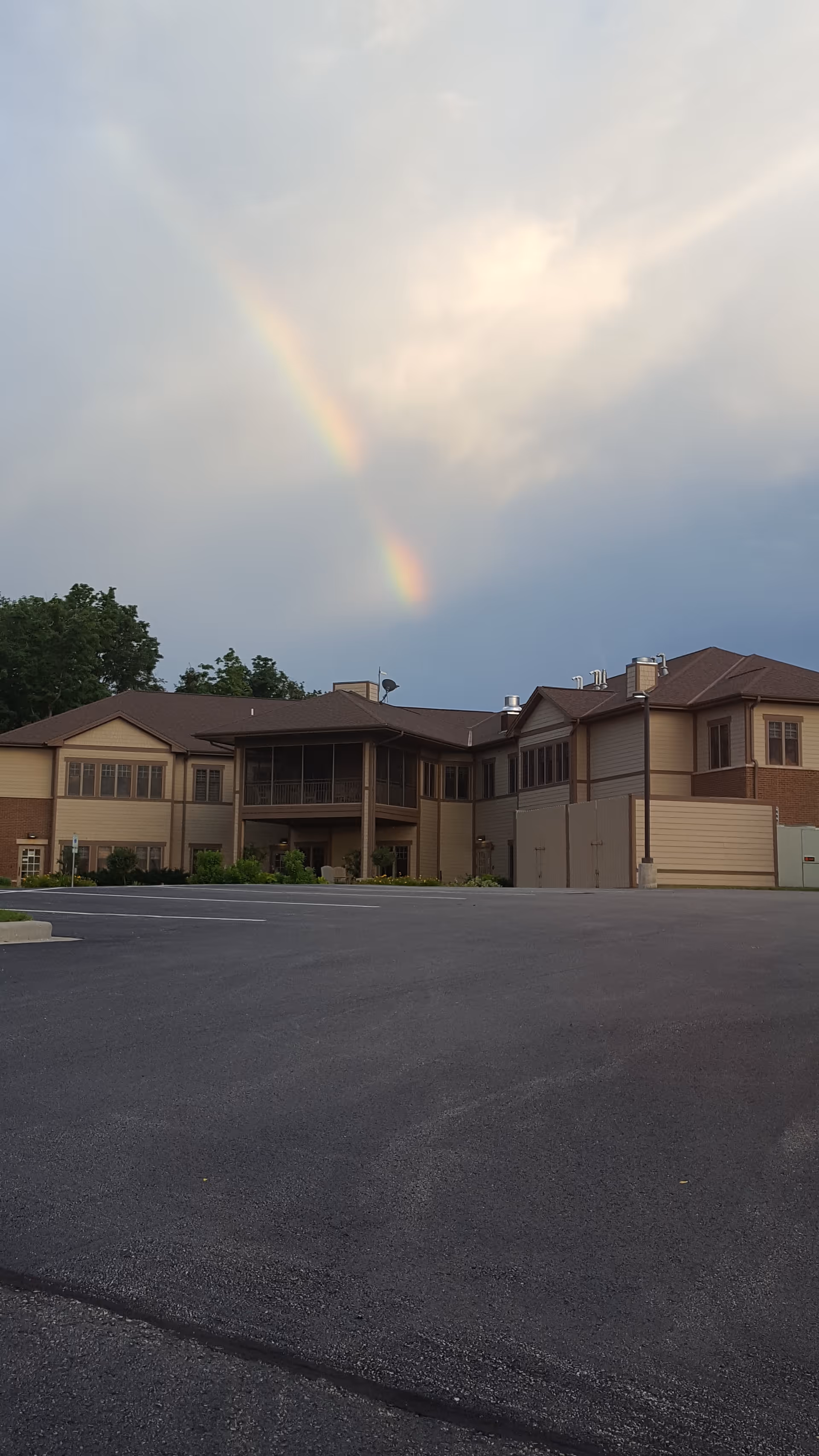Rainbow arches above a two-story beige senior living building with a paved parking lot.