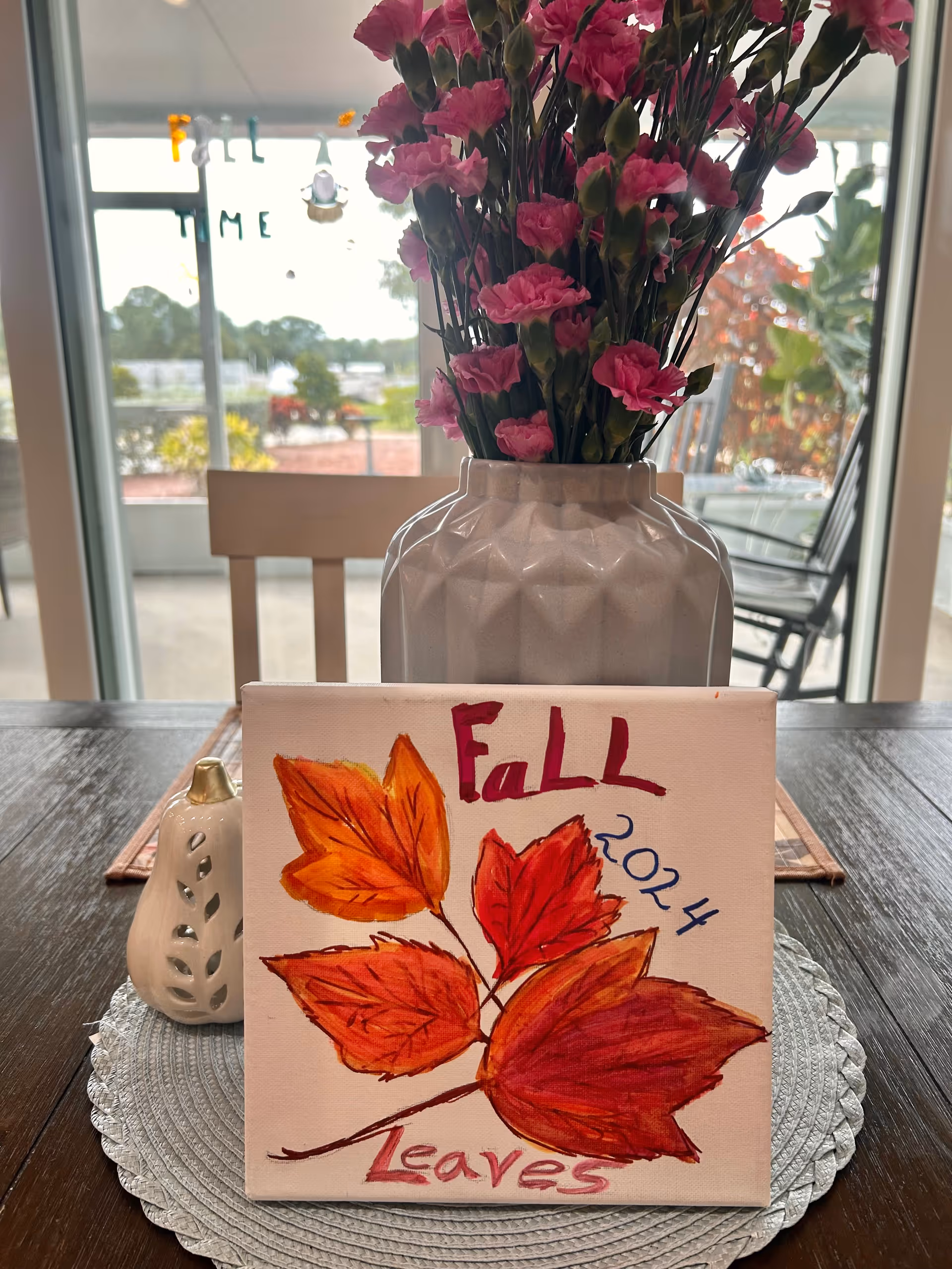 Decorative interior table with a pink flower vase and a leaf-themed Fall Leaves painting.