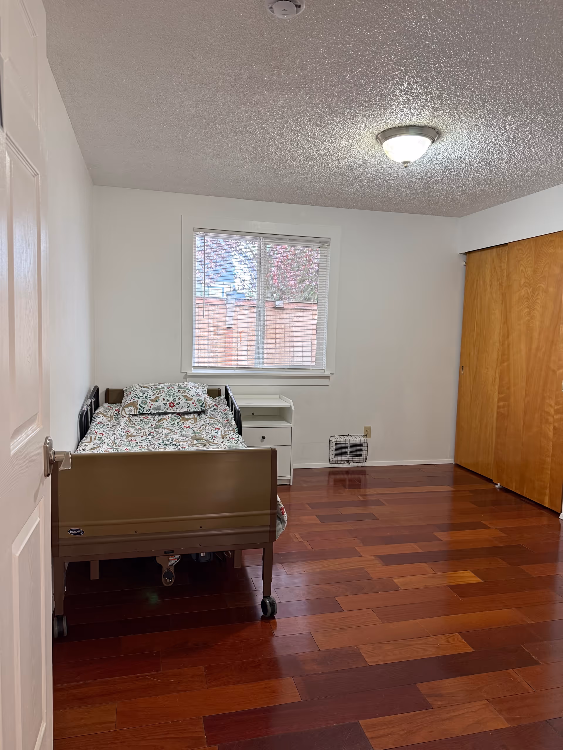 Small bedroom with a single bed, nightstand, window, and wooden closet doors.