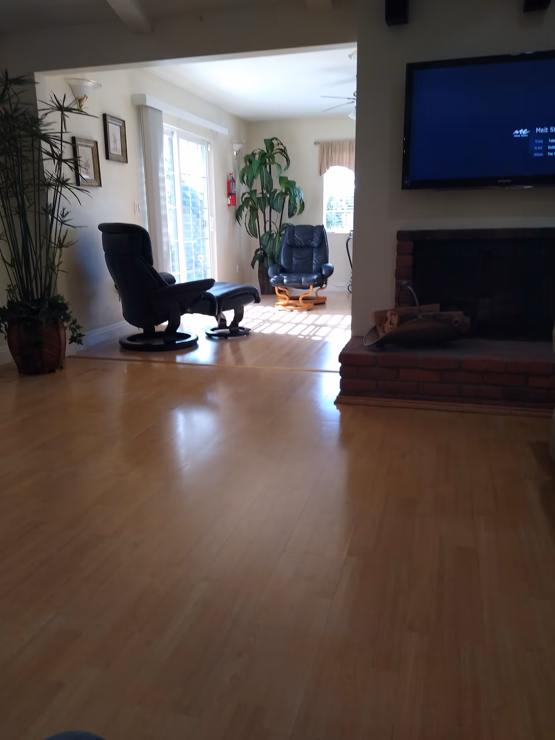 Sunlit living room with recliners, a fireplace, and a large flat-screen TV.