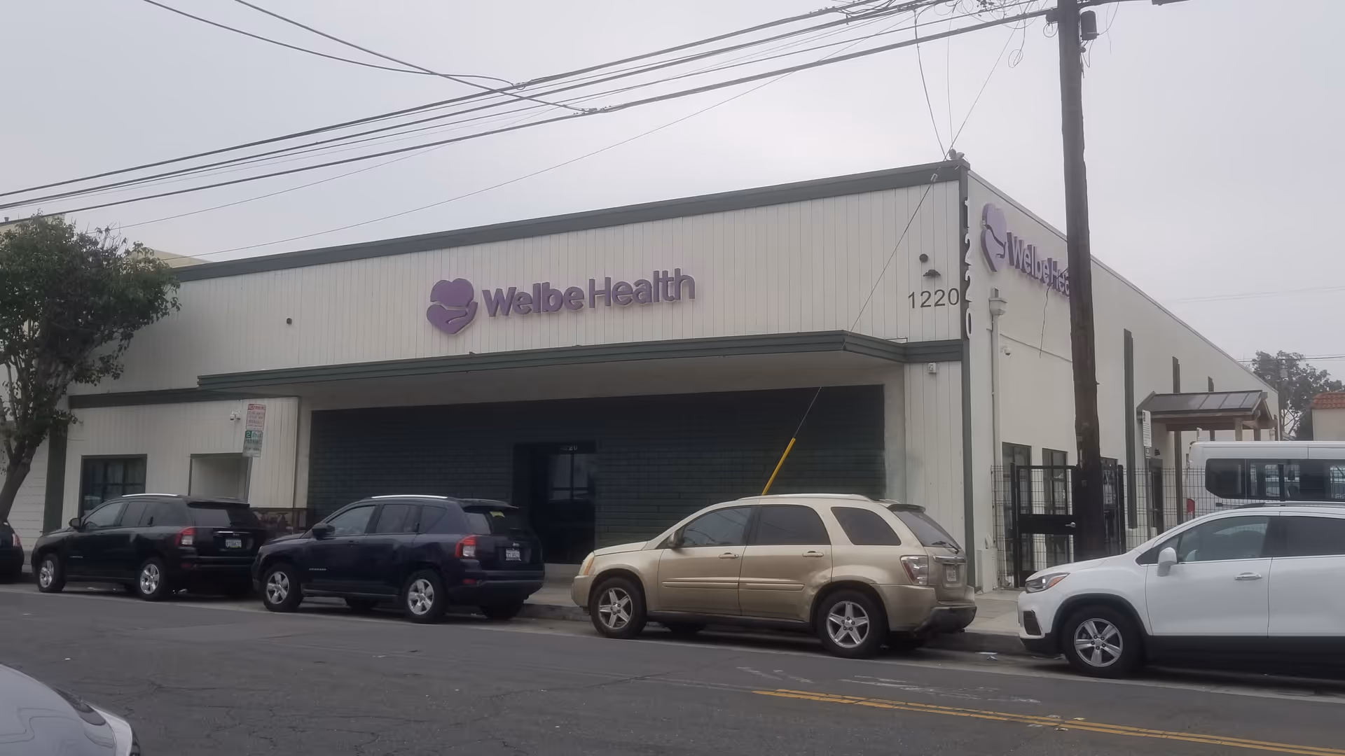 Exterior view of WelbeHealth building with parked cars along the street