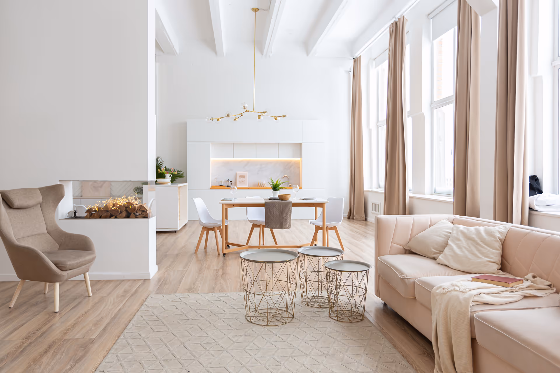 Bright, modern living and dining area with beige sofa, chairs, fireplace, and large windows.