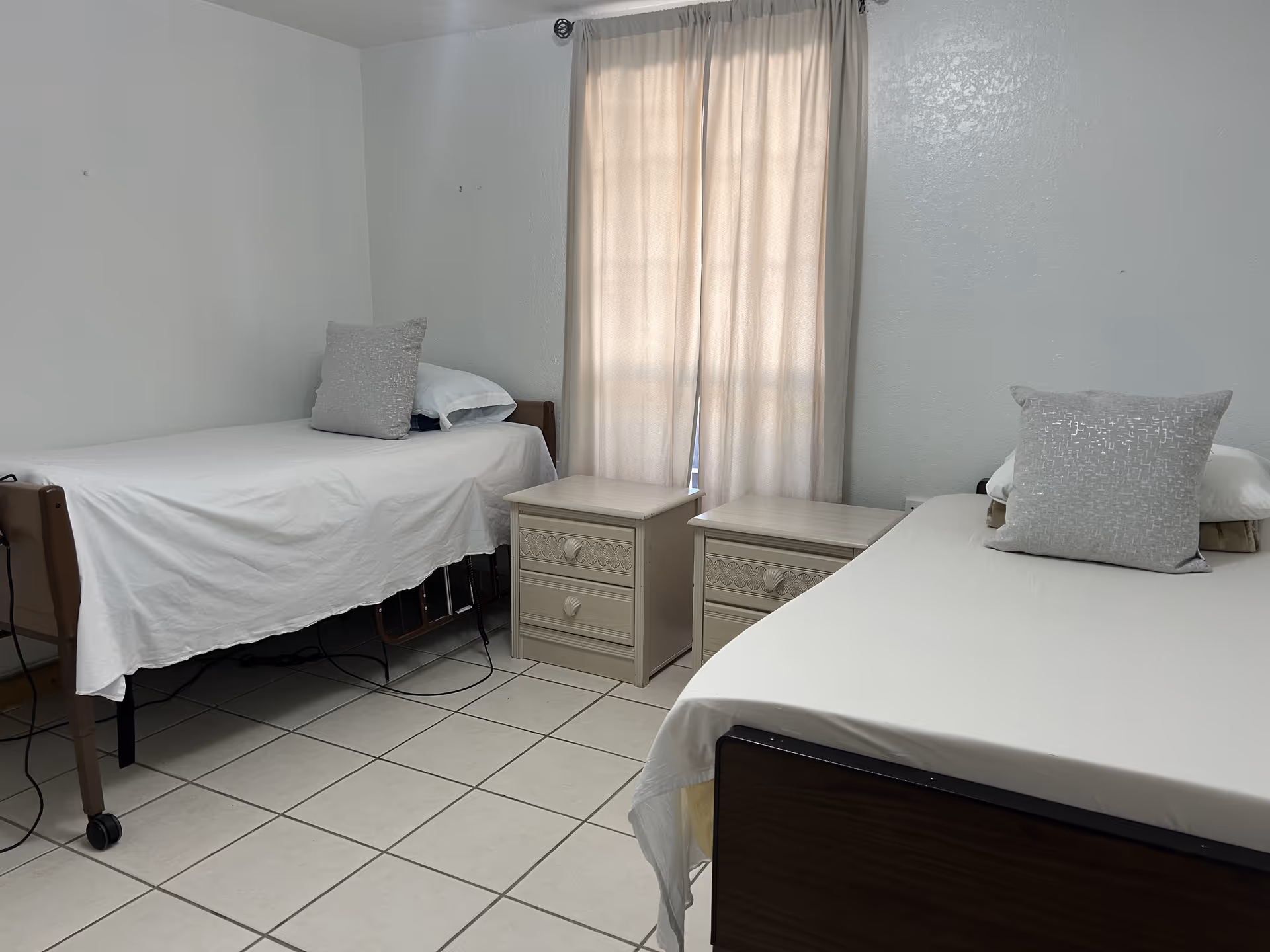 Two single beds with white linens, matching nightstands, and a window with curtains.