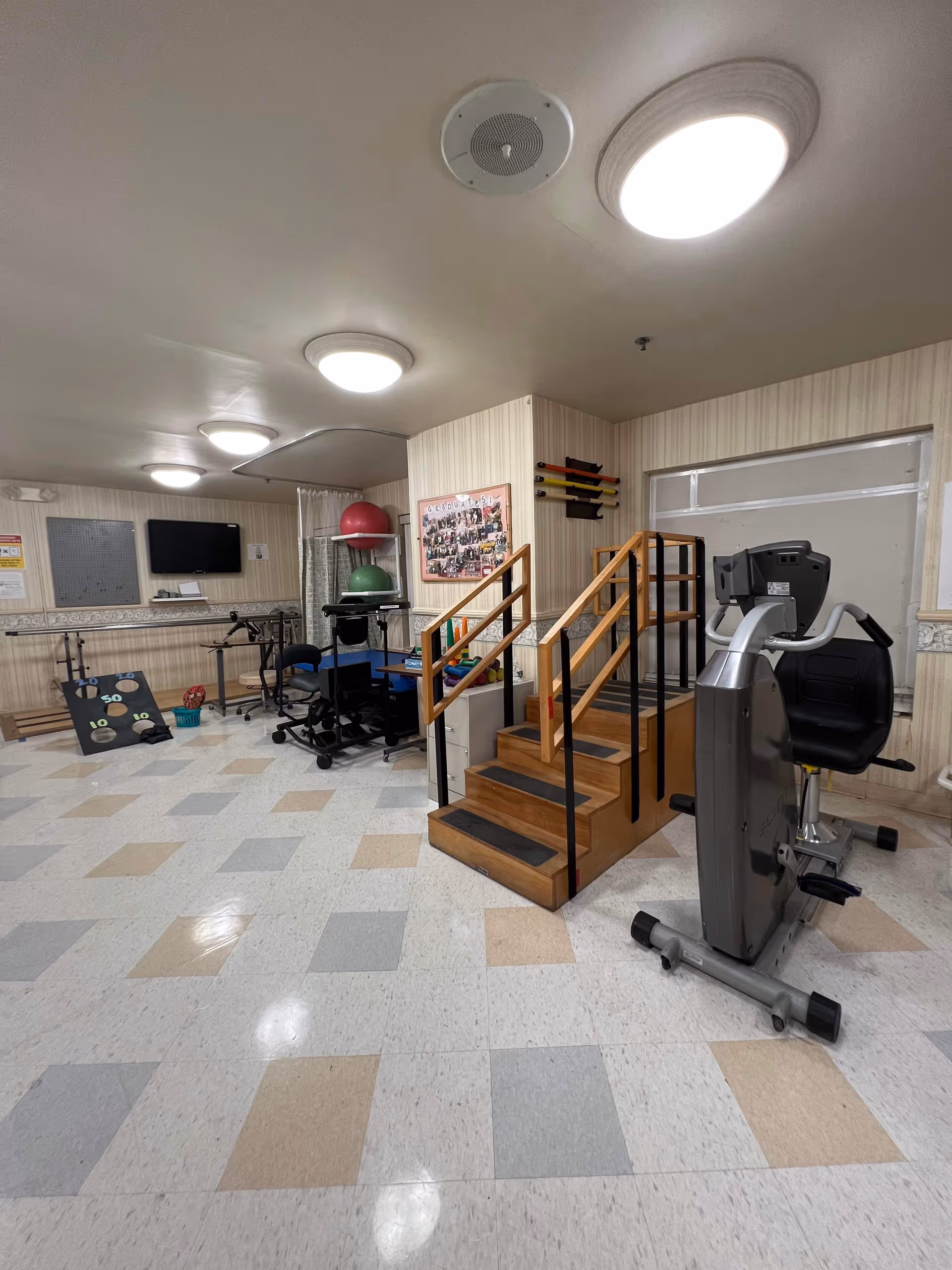 Indoor rehabilitation gym with stairs, exercise machines, and balance equipment.