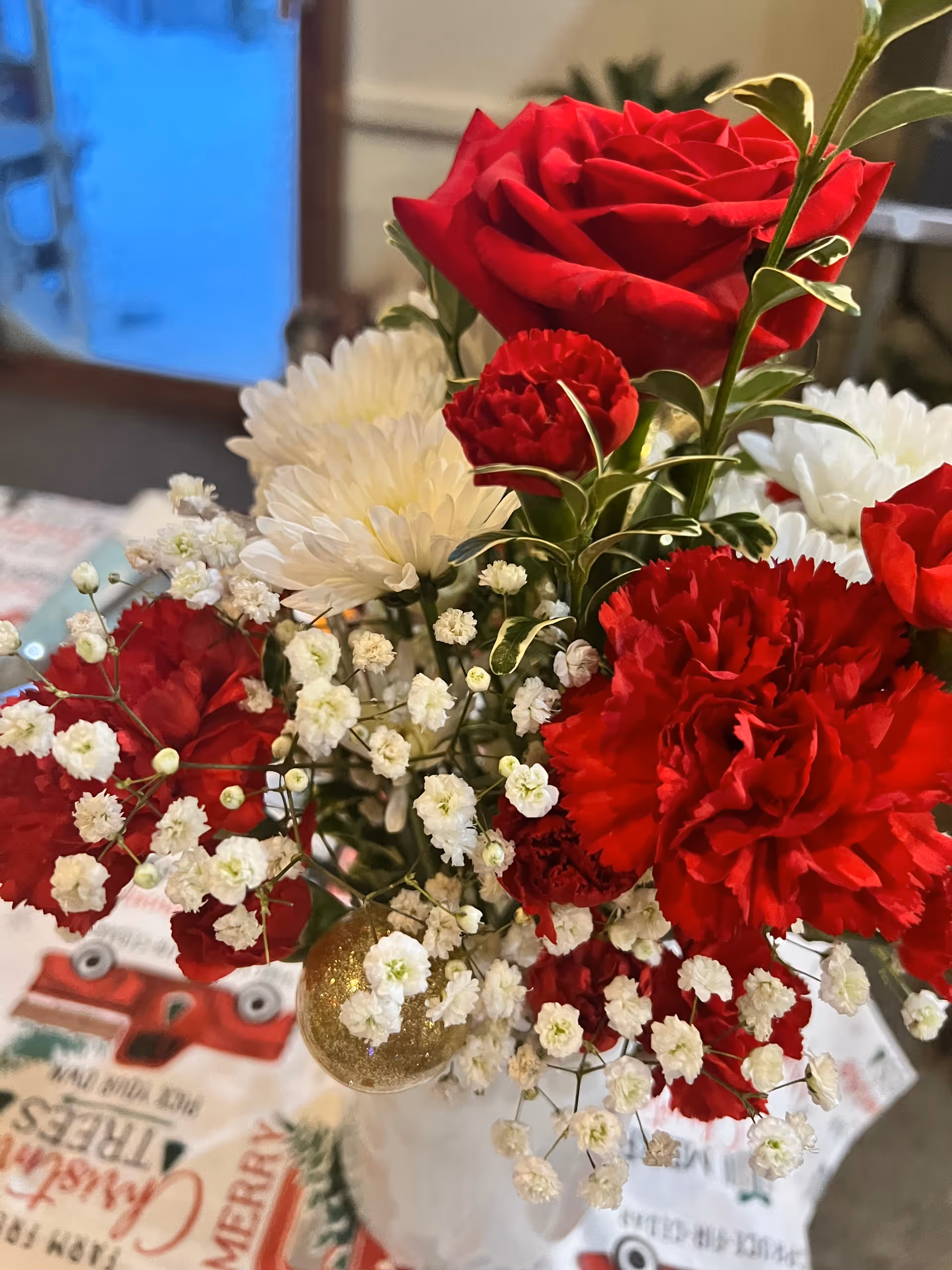 Close-up of a red and white floral bouquet with roses, carnations, and baby's breath on a holiday tablecloth.