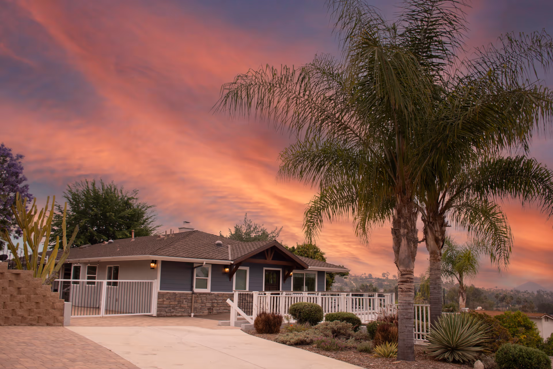 Sunset sky over a single-story assisted living facility with palm trees and landscaped front yard.