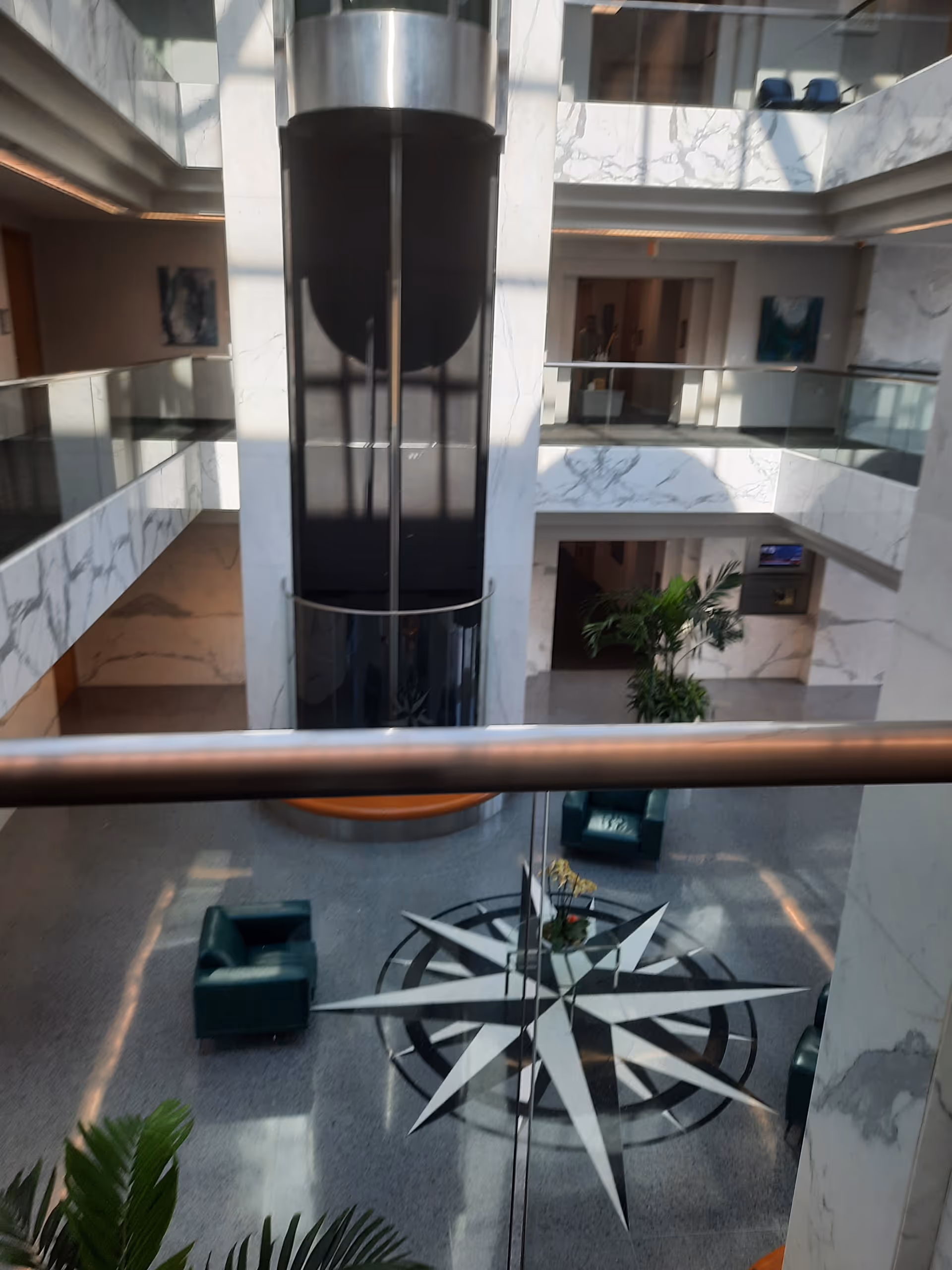 Indoor atrium with marble walls, glass railings, elevator shaft, and a star-shaped floor pattern.