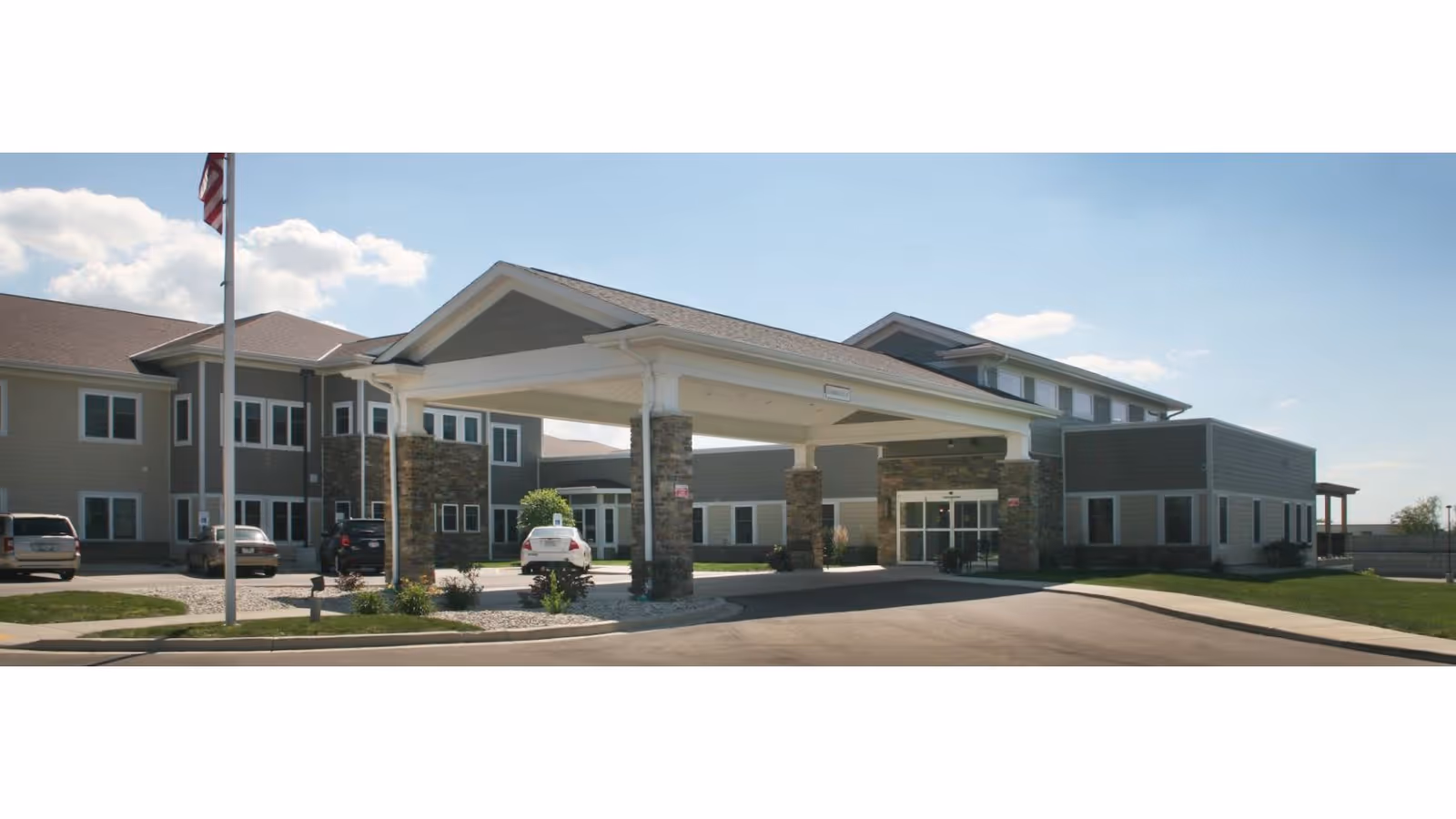 Exterior view of Oak Park Place of Burlington with a covered entrance and parked cars.