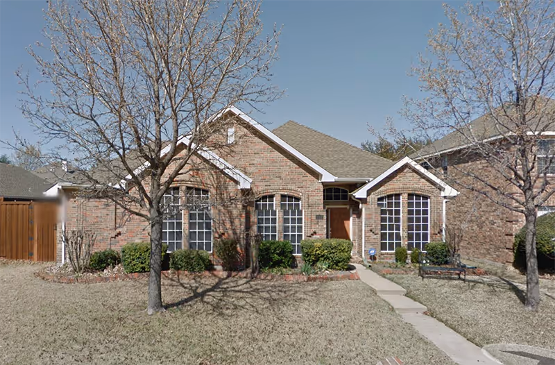 Front view of a brick senior living facility with a walkway and trees.