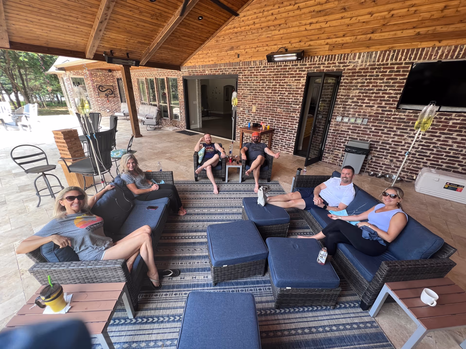Group of adults relaxing on outdoor wicker seating under a covered patio.