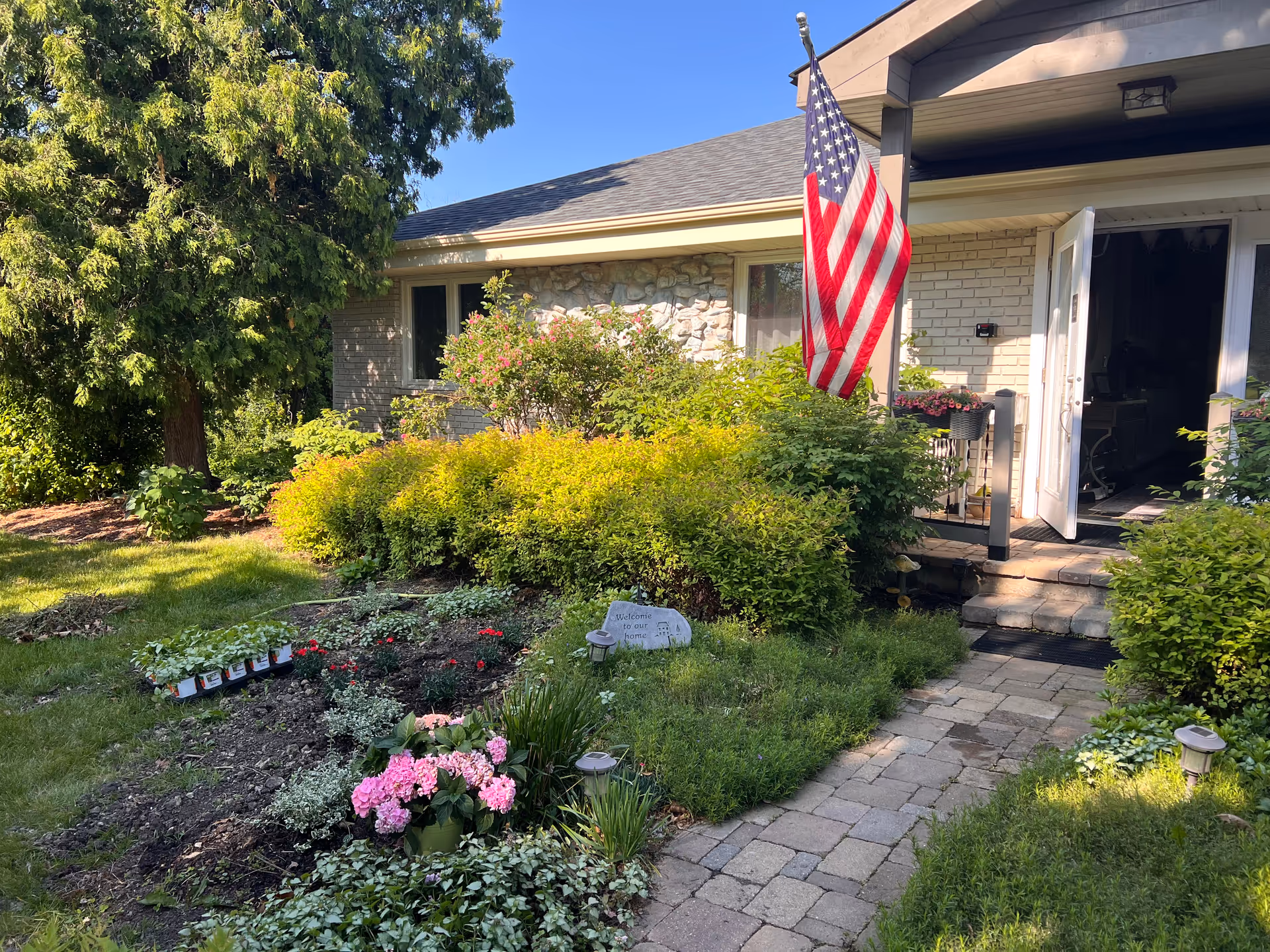 Front entrance of a senior living home with garden, flag, and walkway.