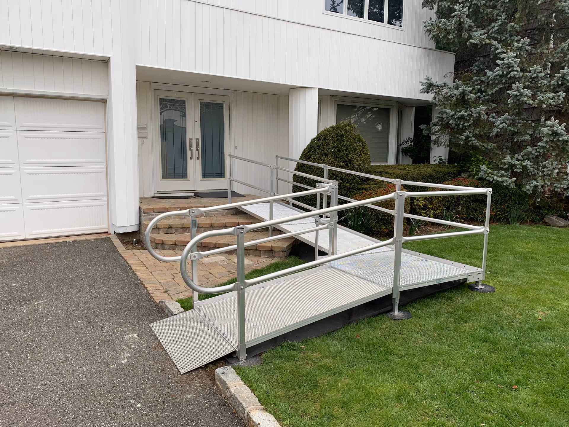 Front exterior of a senior living facility with a metal wheelchair ramp to double doors.