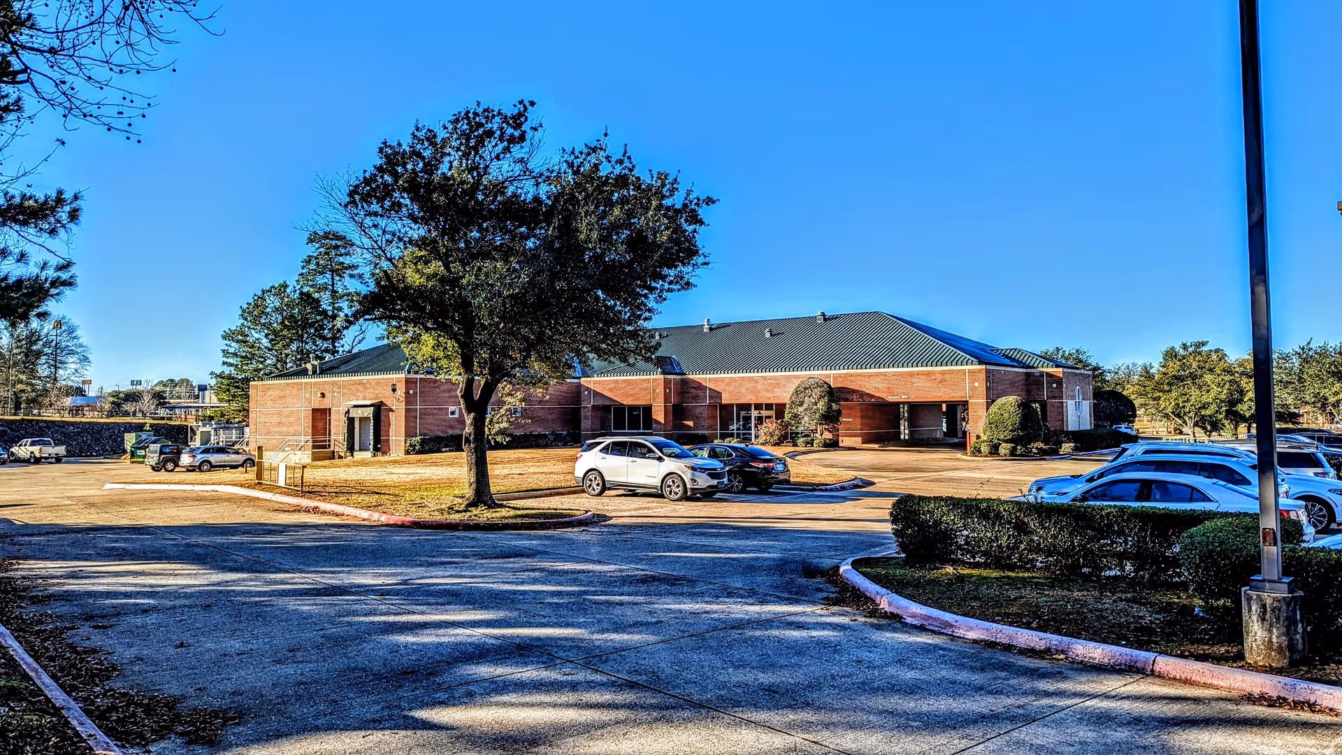 Exterior view of a brick Texarkana Surgery Center with parked cars and trees.