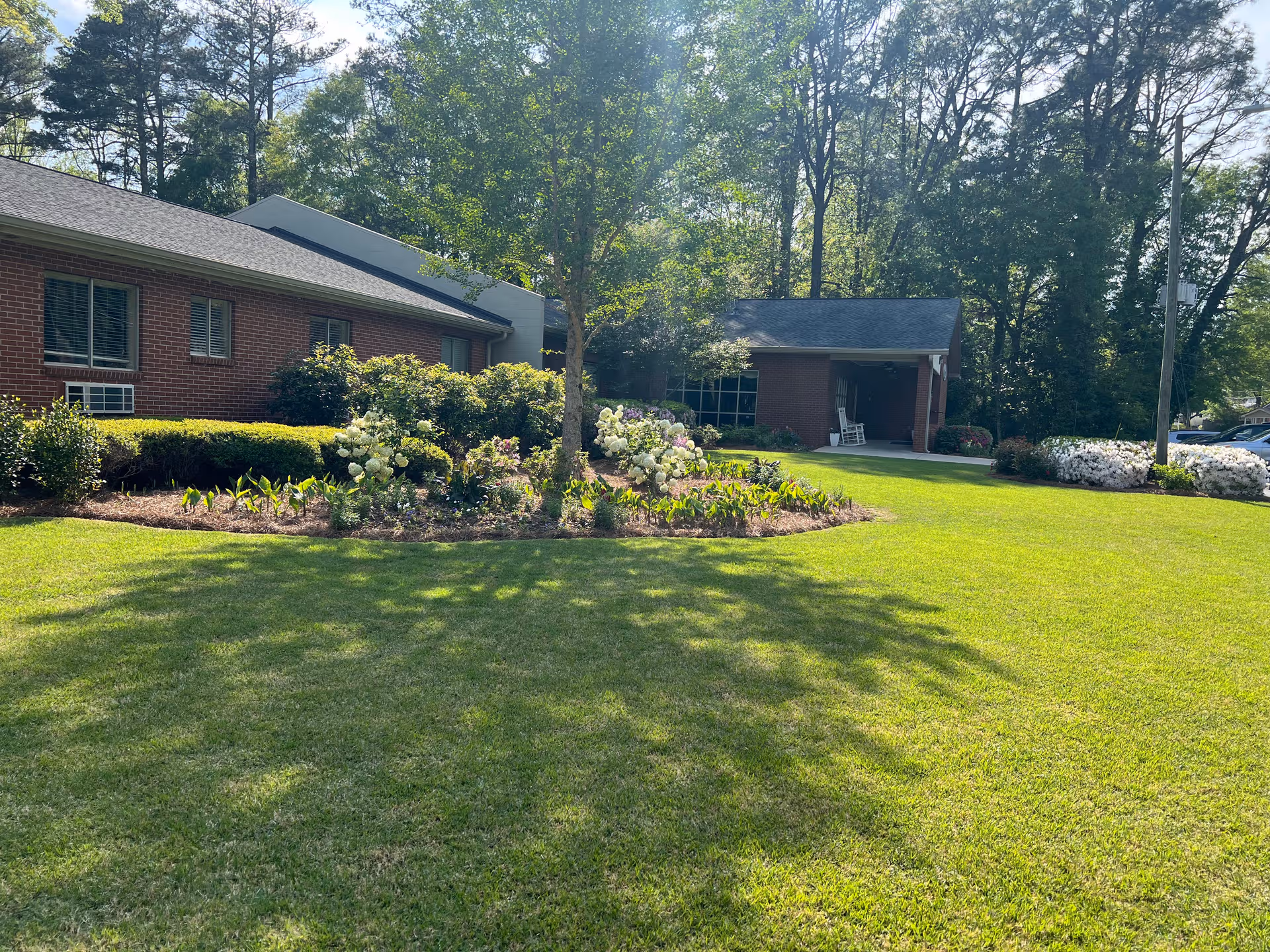 Brick senior living facility exterior with manicured lawn and flowering shrubs near entrance