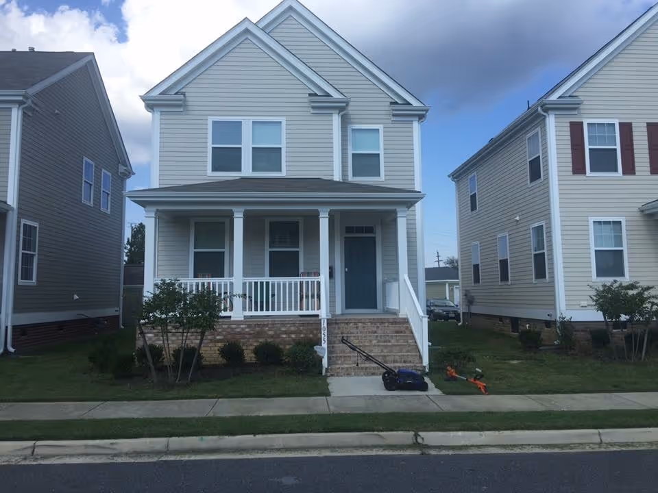 Two-story beige house with a front porch on a residential street.