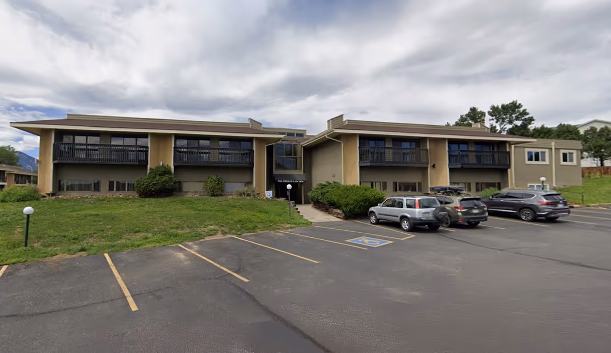A two story beige senior care building with balconies and a parking lot in front.