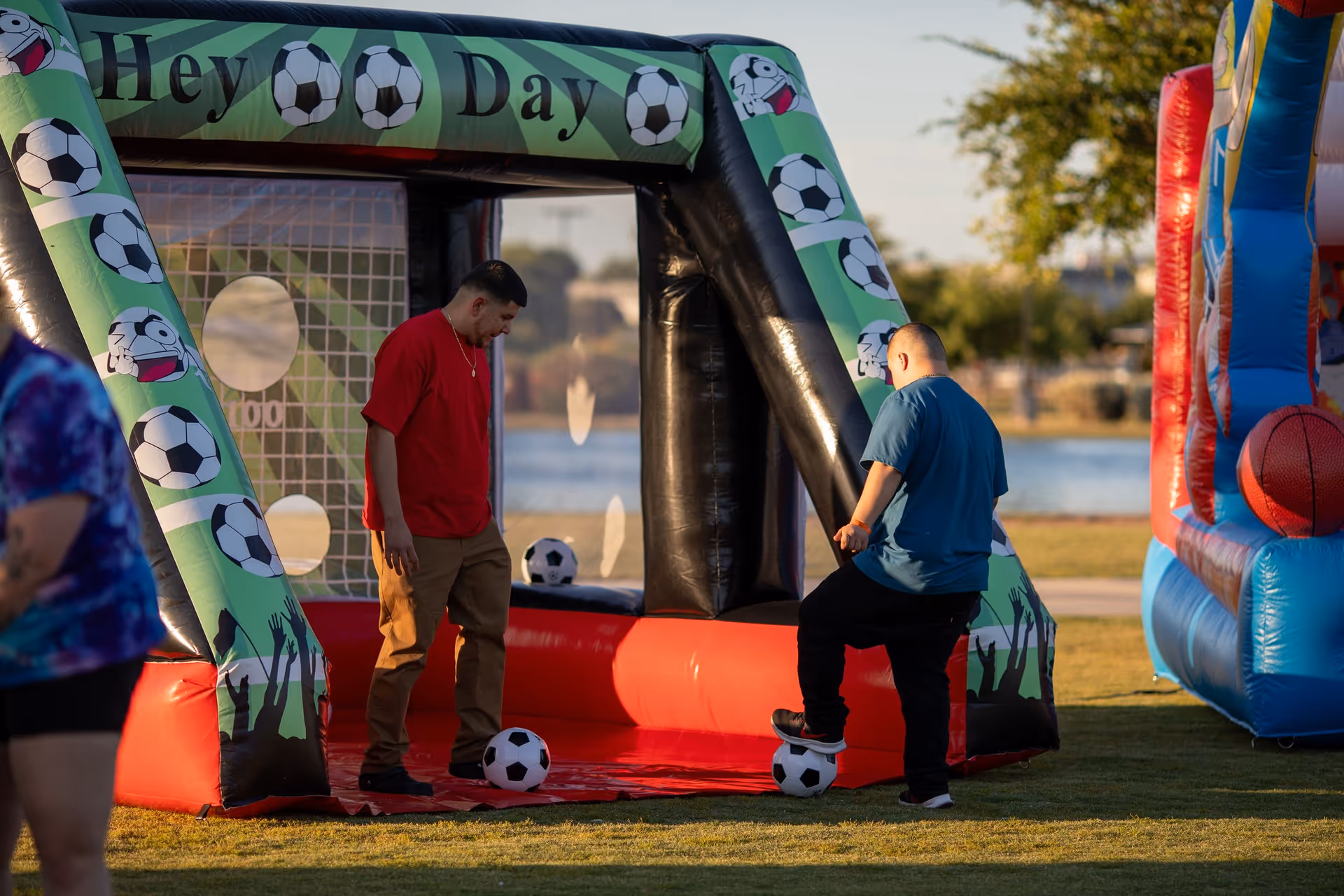 Outdoor inflatable soccer game with two men playing near a waterfront.