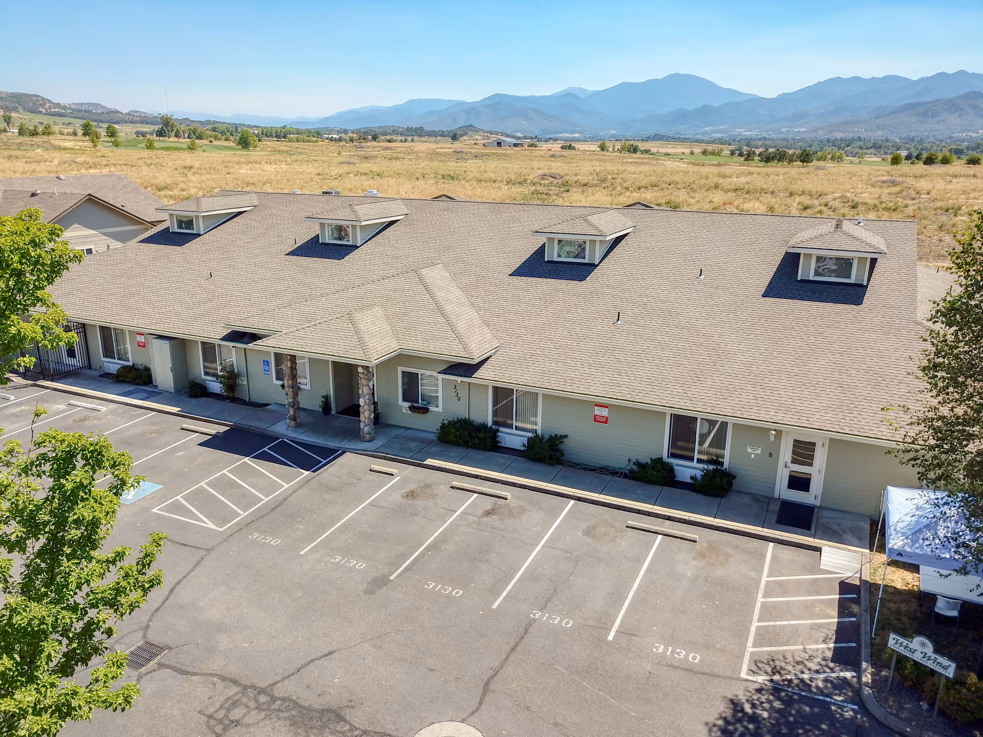 A single-story senior living facility with a long front, parking lot, and surrounding mountains.