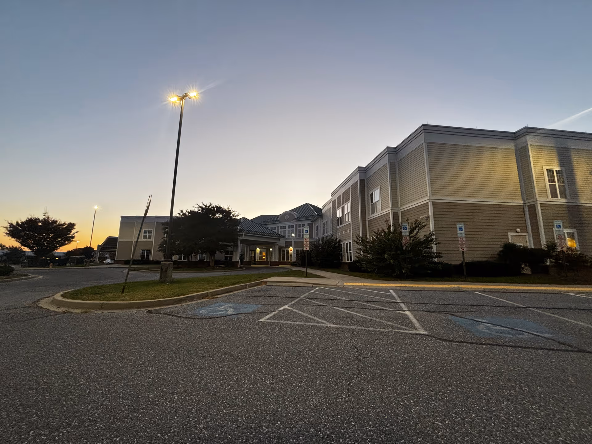 Exterior front of a two-story assisted living building at dusk with a parking lot and illuminated streetlights.