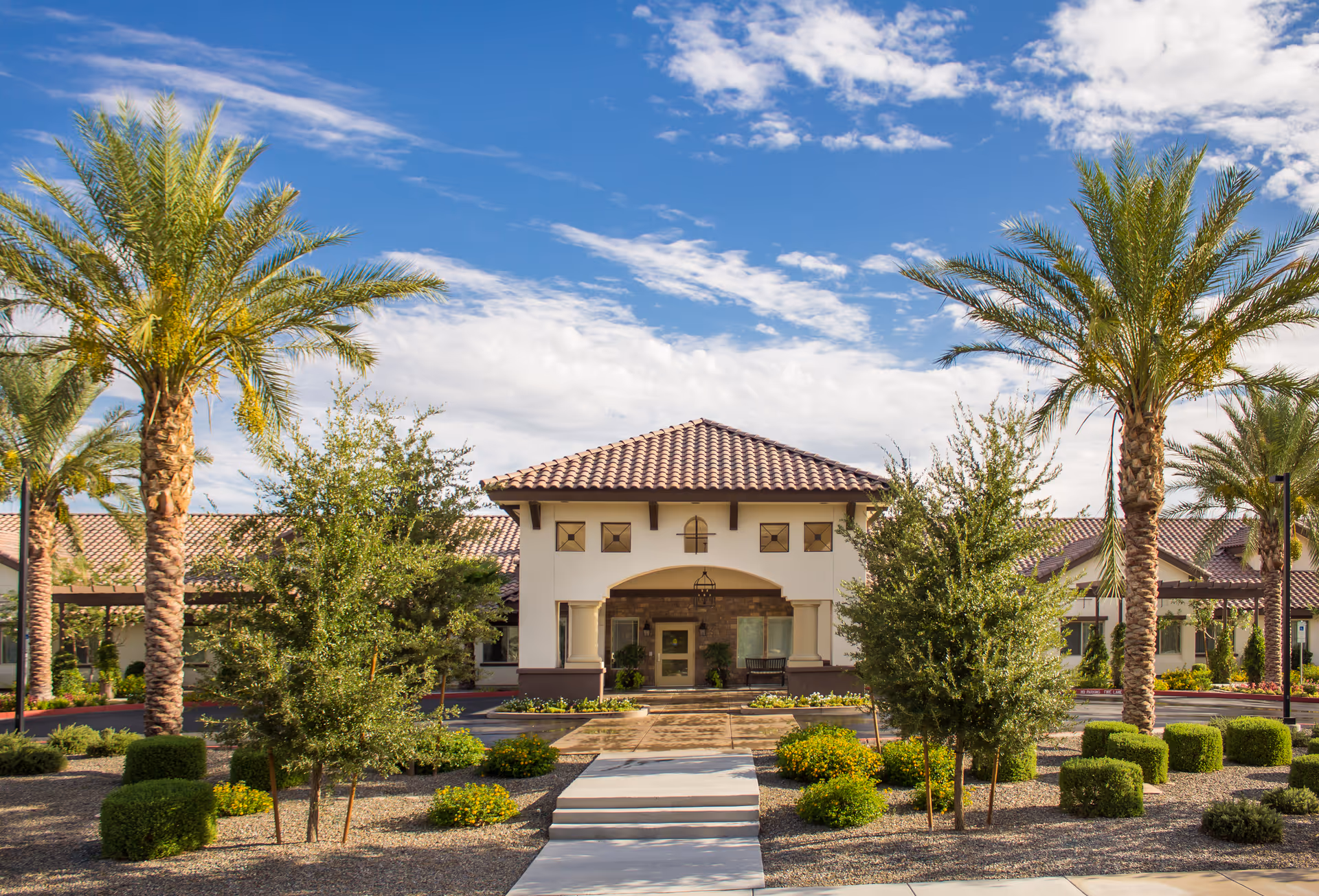 Front view of The Gardens at Laguna Springs exterior with a tiled roof and palm trees.