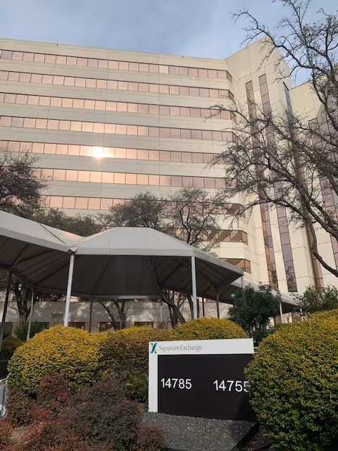 Tall beige building with pink-tinted windows, front canopy, and a sign at the entrance.