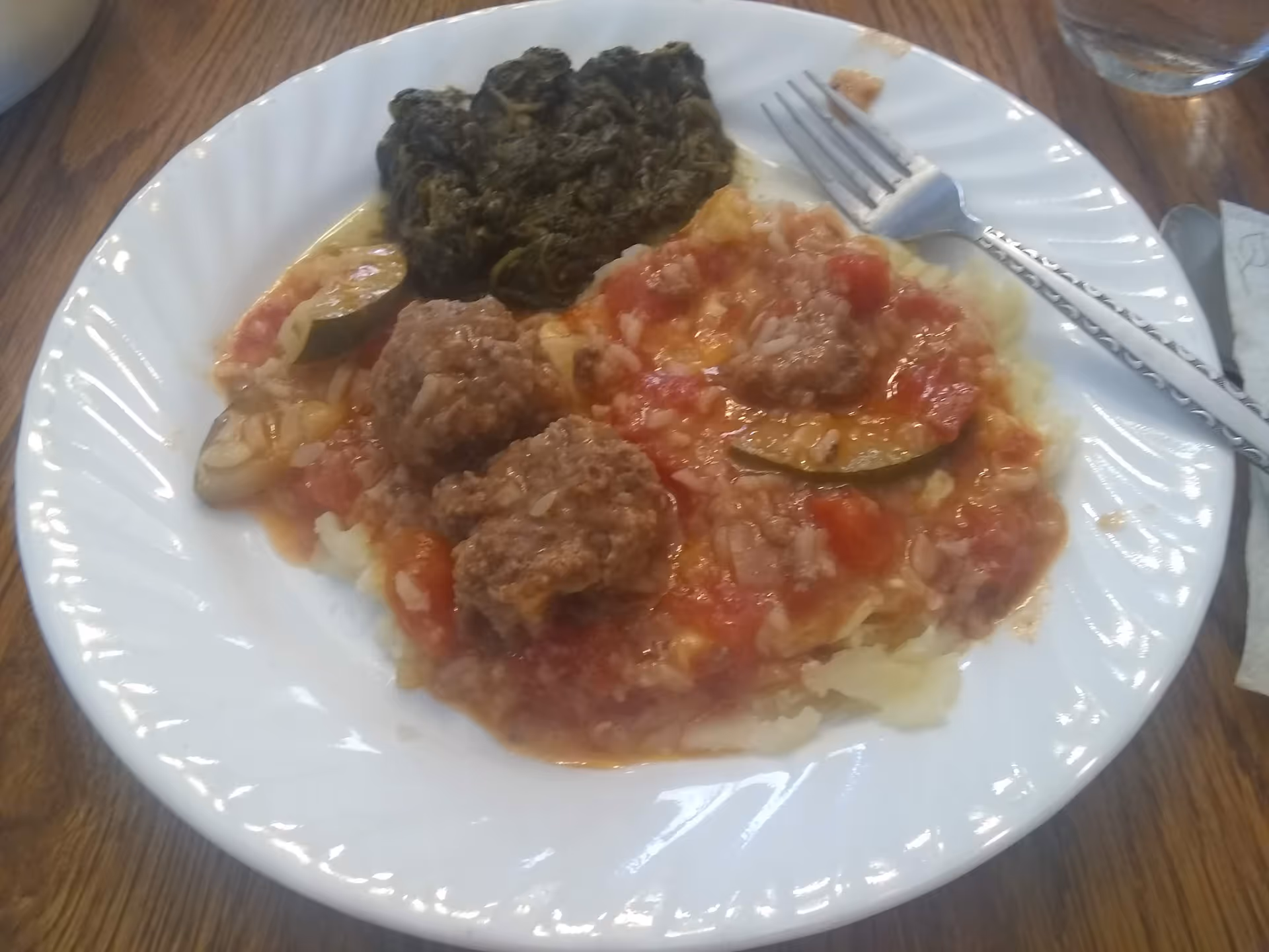 Plate of meatballs in tomato sauce with vegetables on a white dining plate.