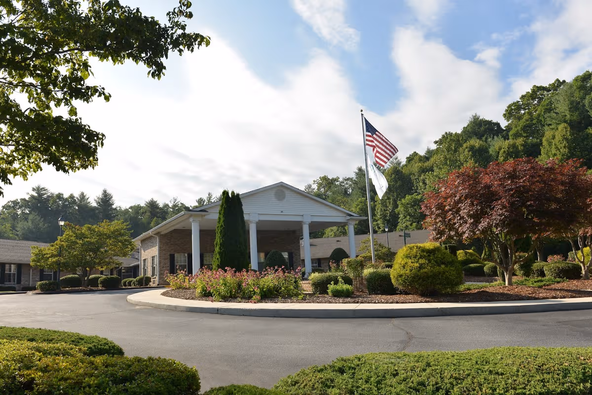 Front view of The Laurels of Hendersonville entrance with flags and landscaped driveway.