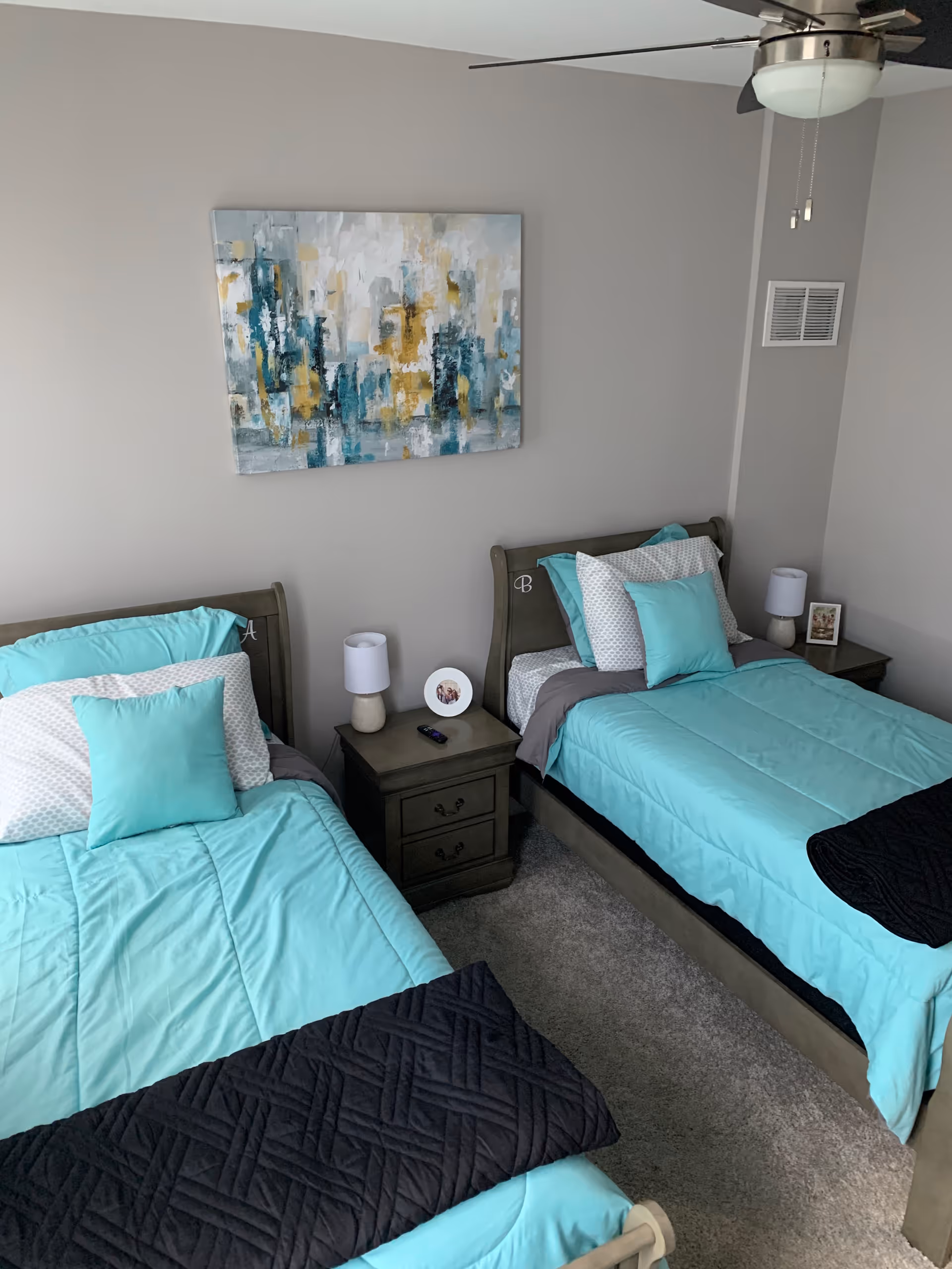 Two twin beds with turquoise bedding and matching nightstands flank a gray-walled bedroom.