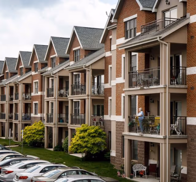 Row of brick senior living apartments with balconies and parked cars.