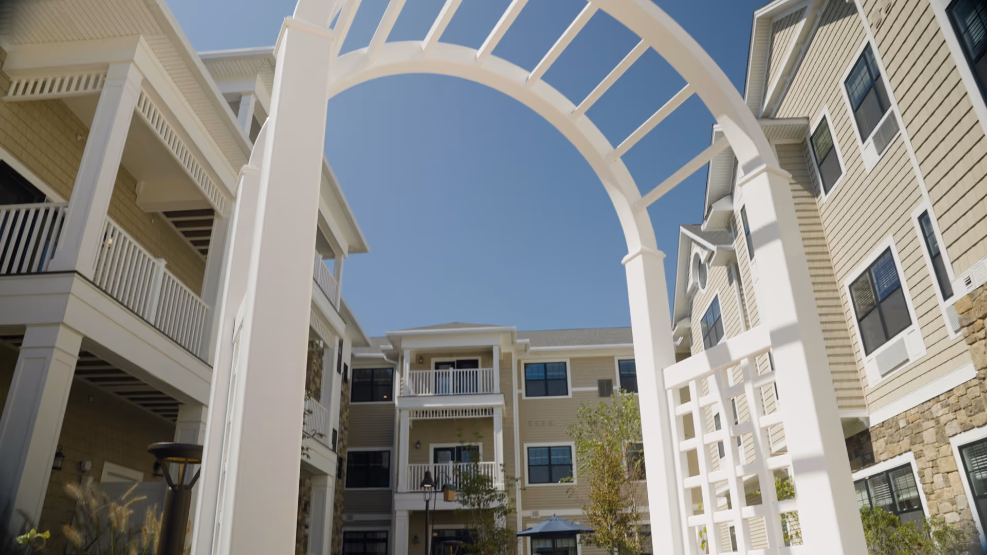 White archway frames beige apartment-style senior living building with balconies and blue sky.