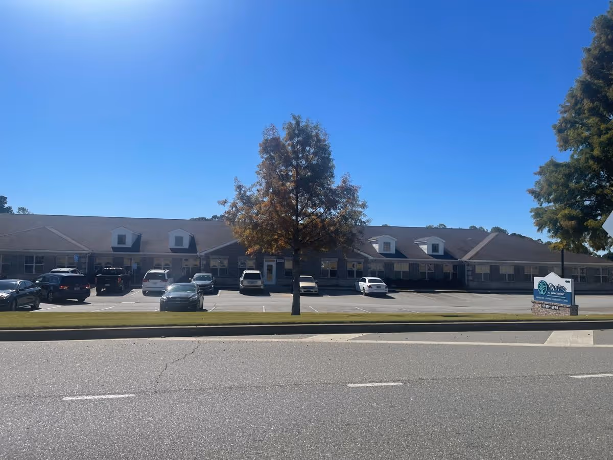 Exterior front view of the Oaks at Gracemont single-story building with a parking lot, trees, and a sign.