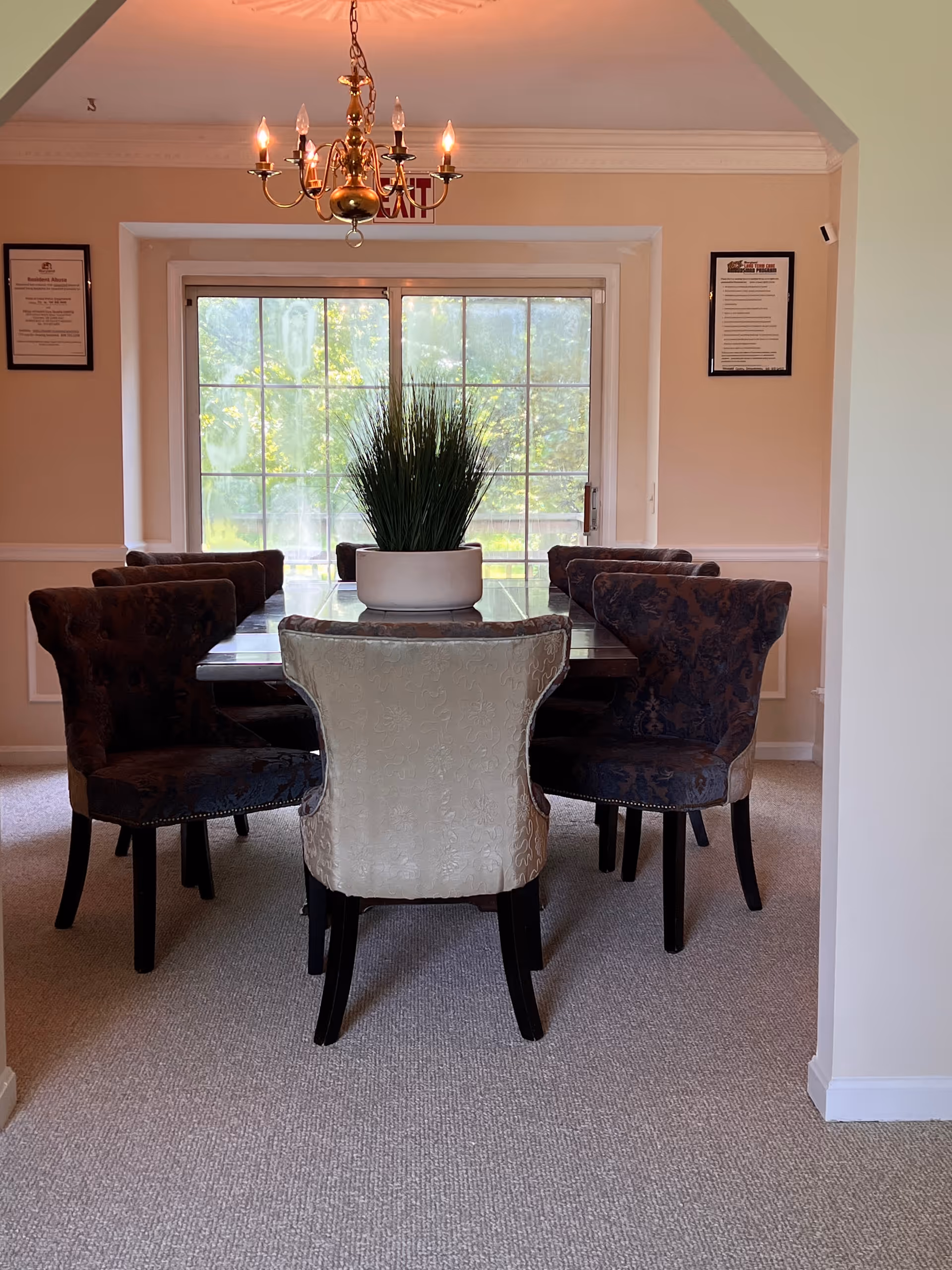 Elegant dining room with a long table, upholstered chairs, chandelier, and large window.