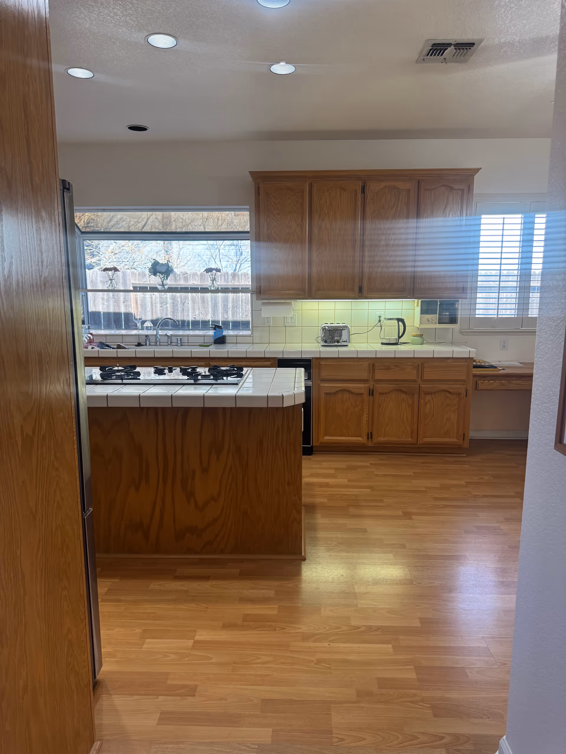 Kitchen with island, tiled counters, wooden cabinets, and a window view.