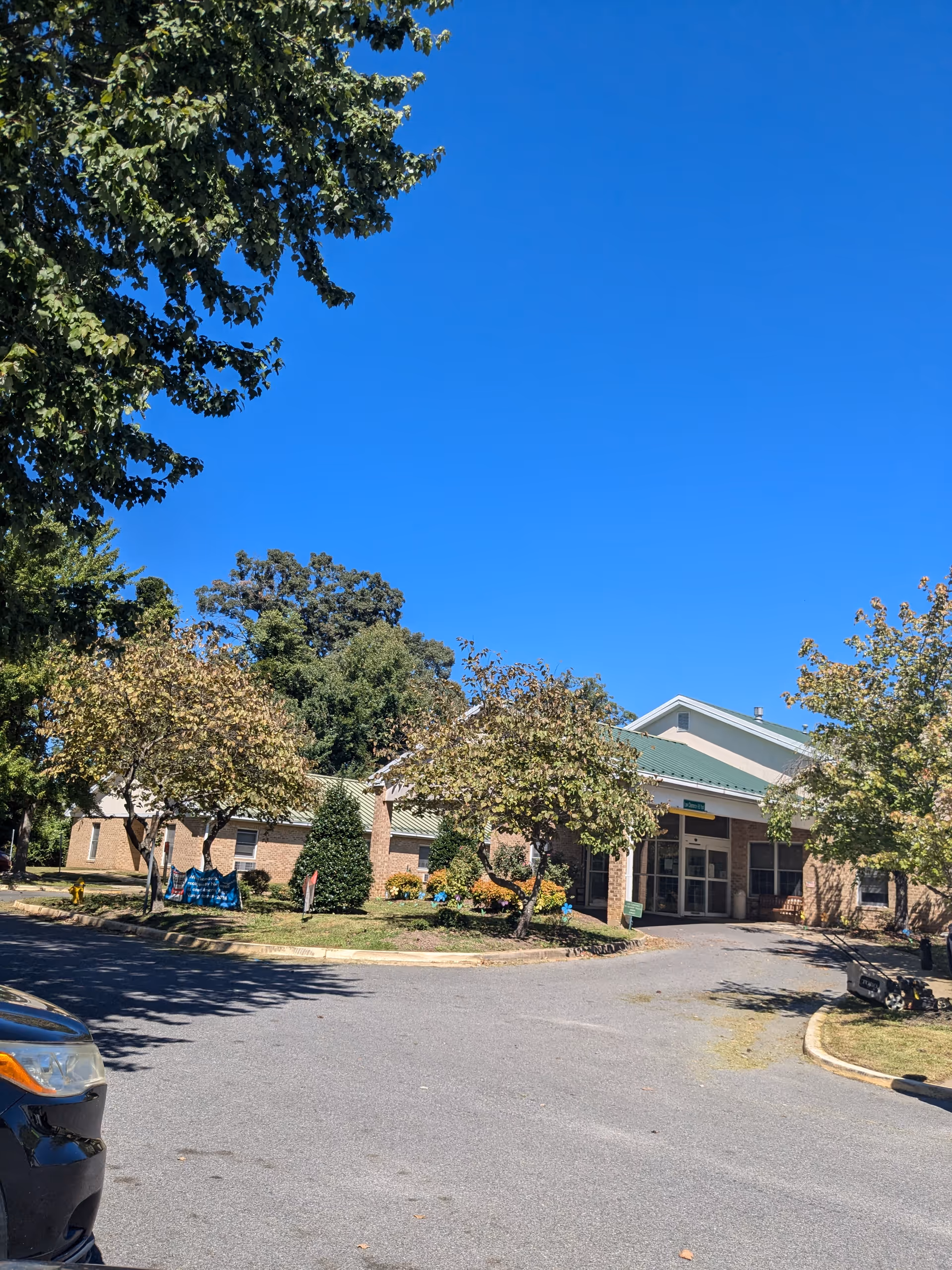 Exterior view of a single-story senior living building with trees and a driveway.