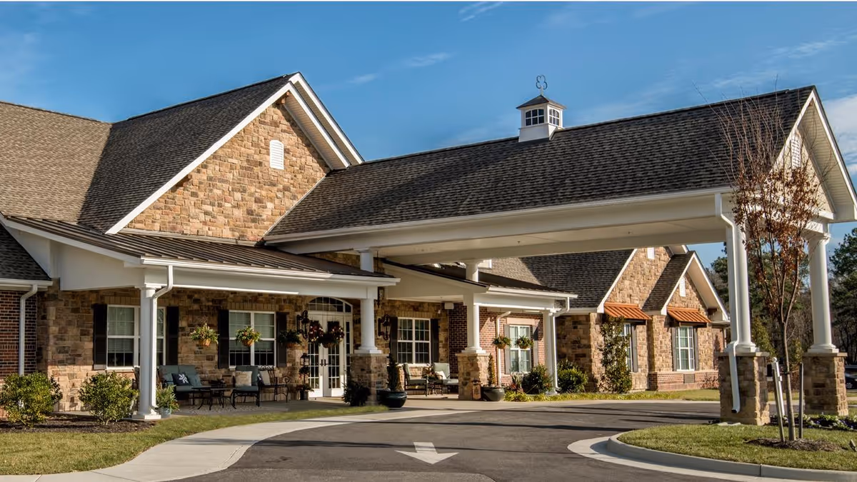 Front entrance of a brick-and-stone senior living facility with a covered porte-cochere and landscaped driveway.