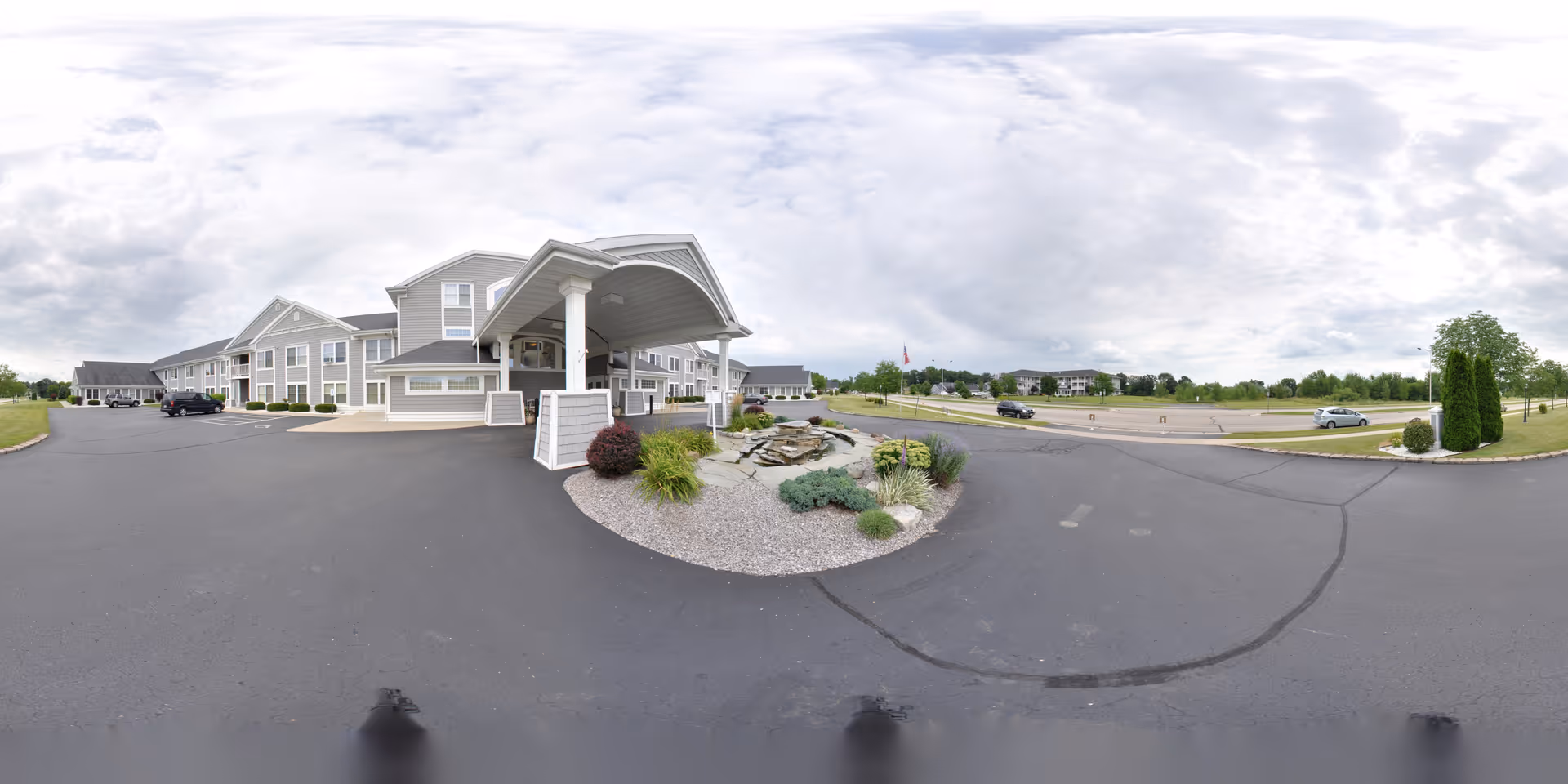 Front exterior of Huntington Place with a covered entrance/porte-cochere, landscaped island, parking area, and cloudy sky.