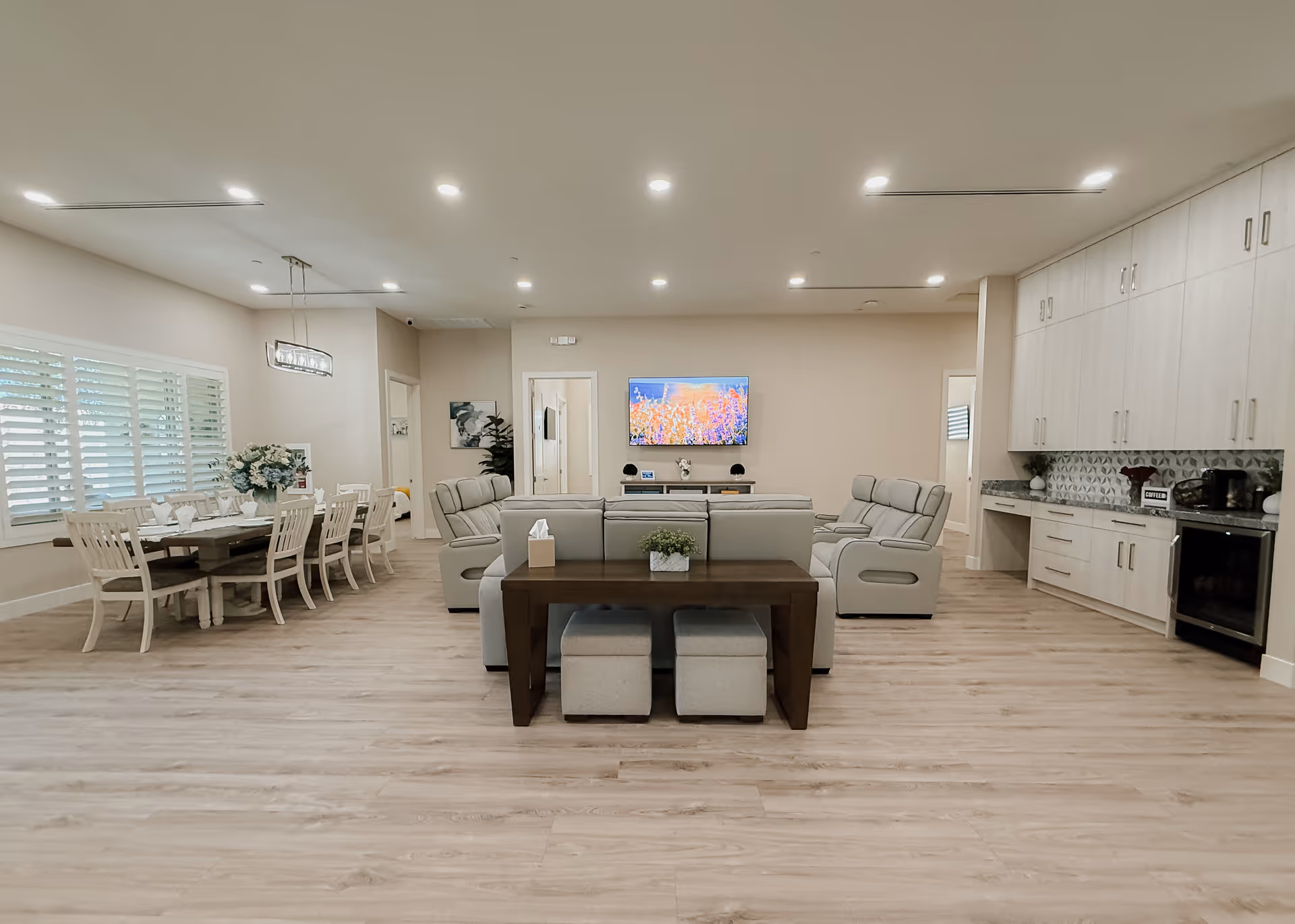 Spacious, modern senior living common area with a dining table, plush seating, and a wall-mounted TV.