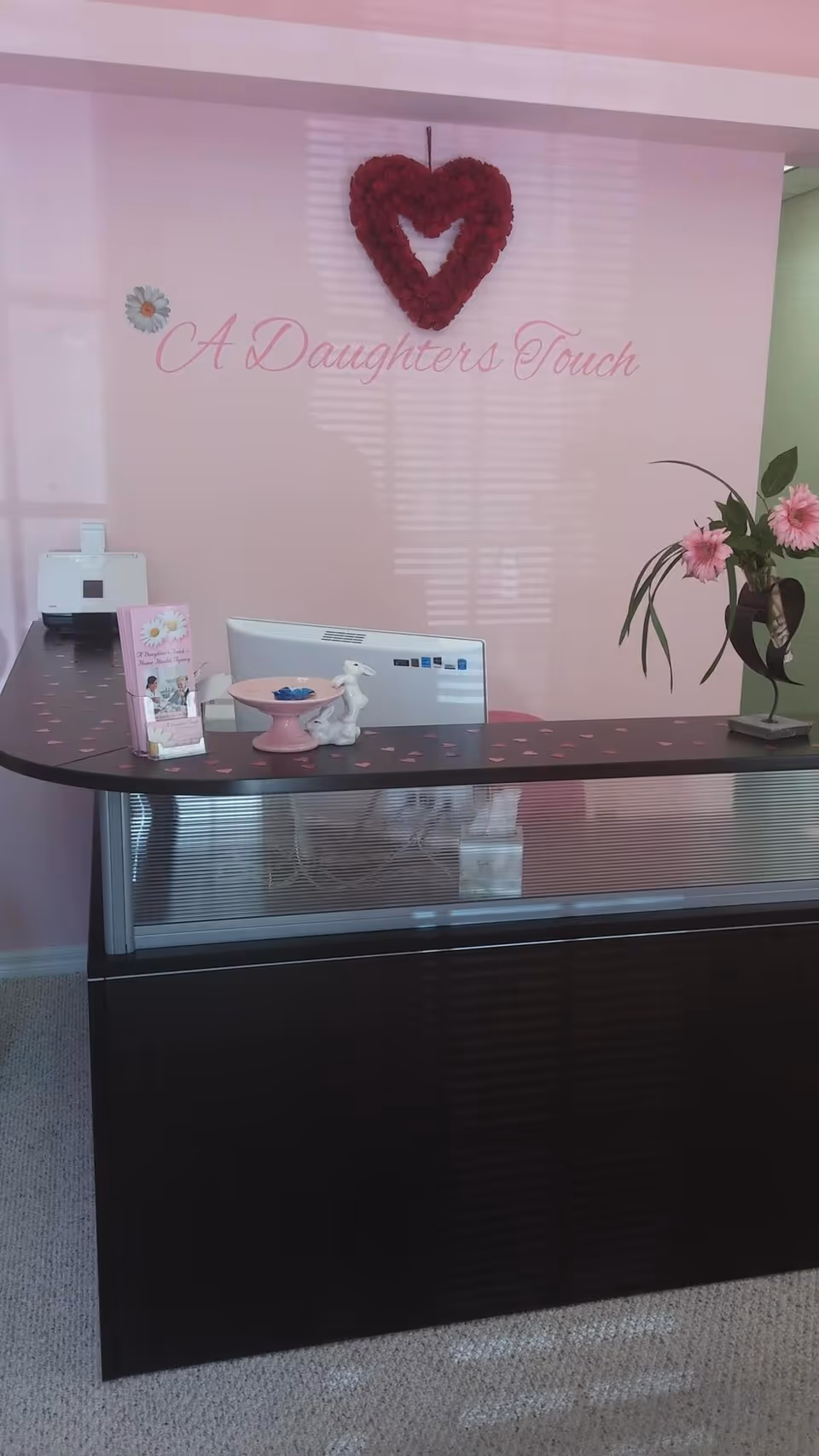 Reception desk in a pink, heart-themed lobby with flowers and the 'A Daughter's Touch' sign.