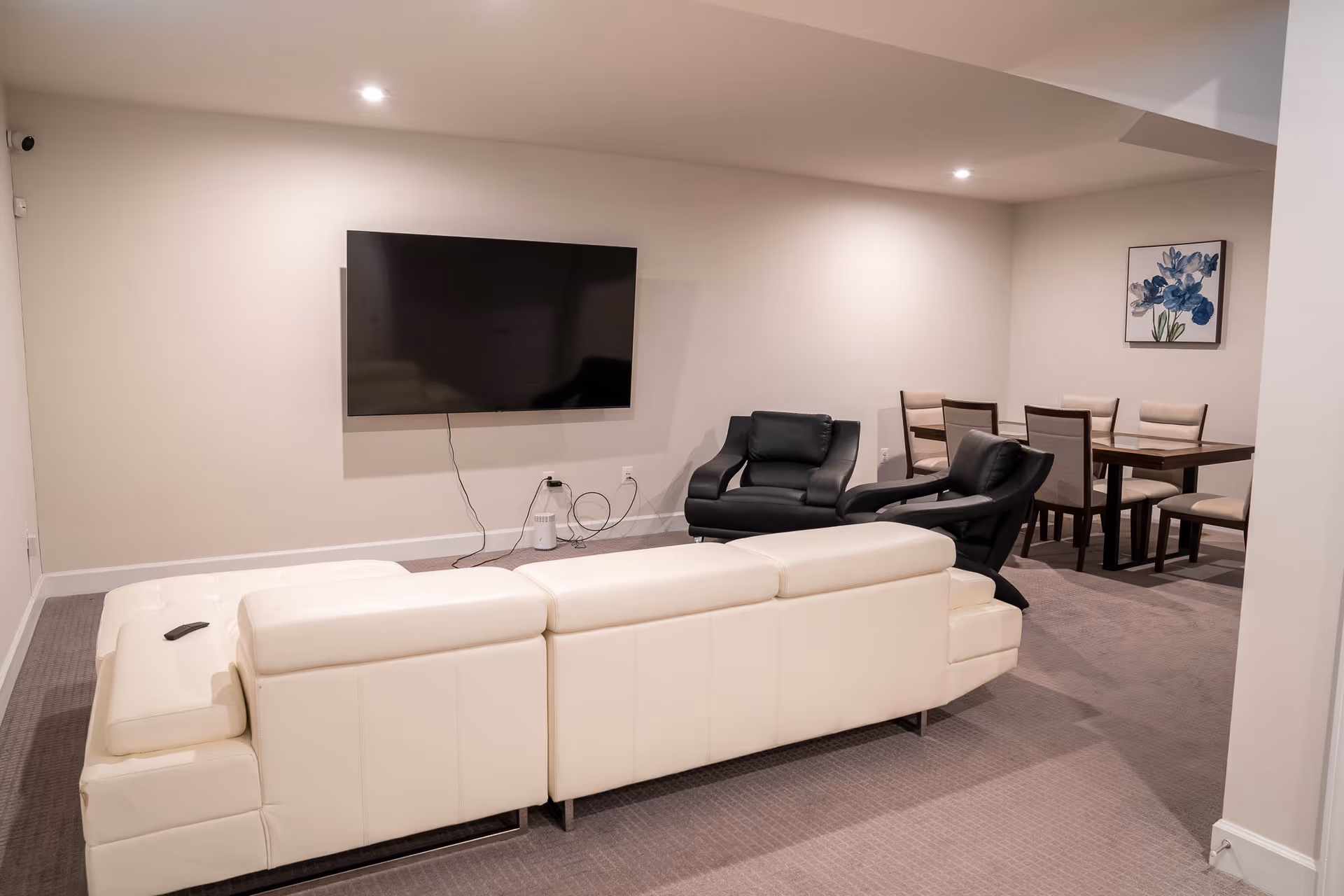 A modern basement-style living room with a white sectional sofa, TV, recliners, and dining area.