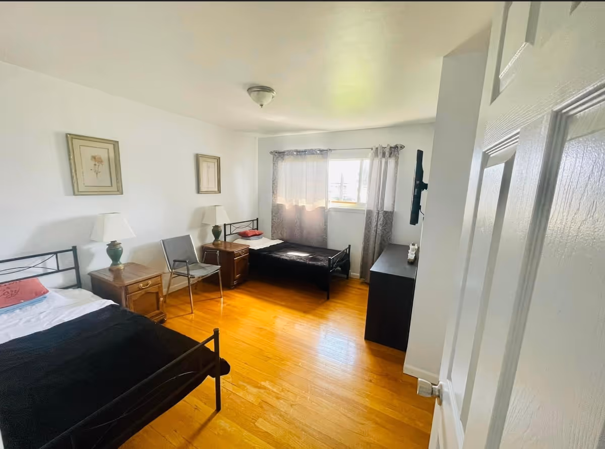 Two single beds with nightstands and chairs in a bright bedroom.