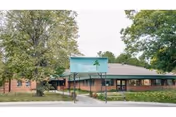 Exterior view of a single-story brick senior living facility with a front sign and trees.