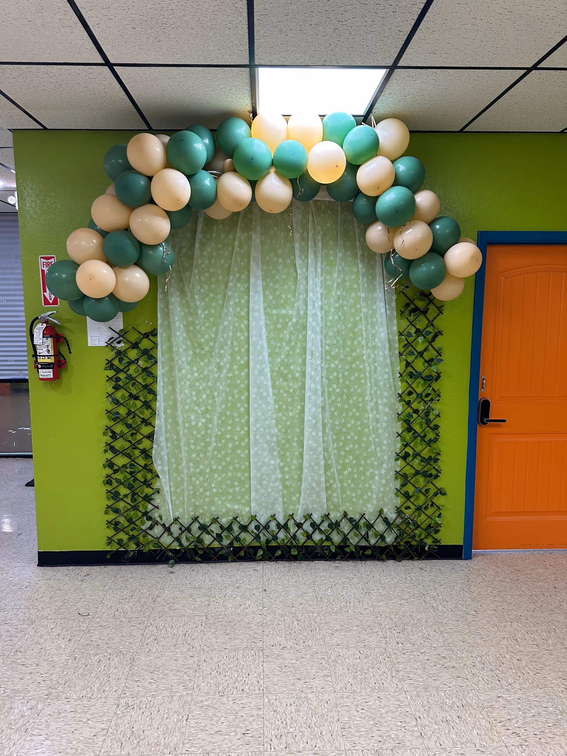 Green hallway with balloon arch above sheer curtain and orange door.