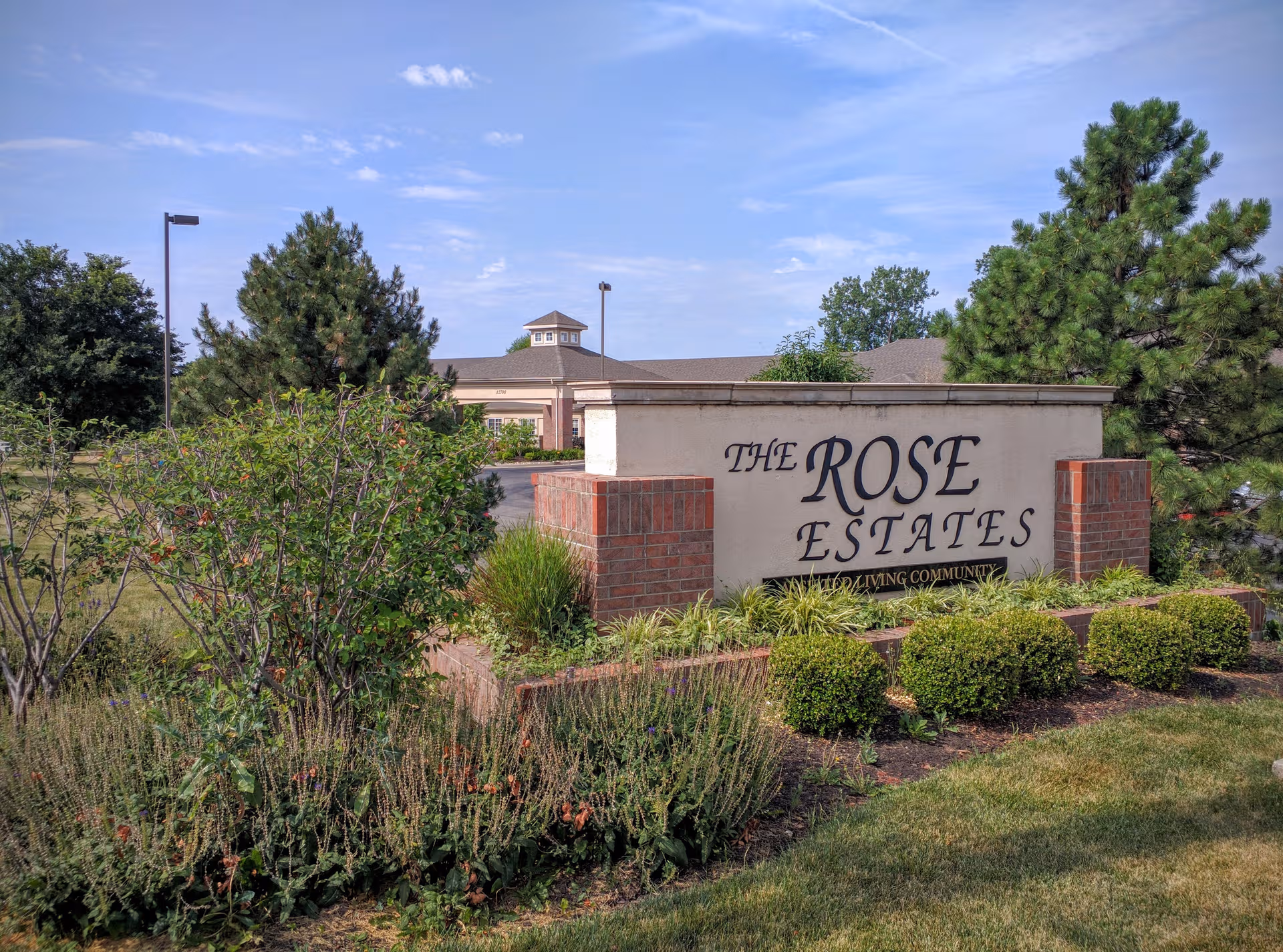 Exterior entrance sign for The Rose Estates senior living community with landscaped foreground.