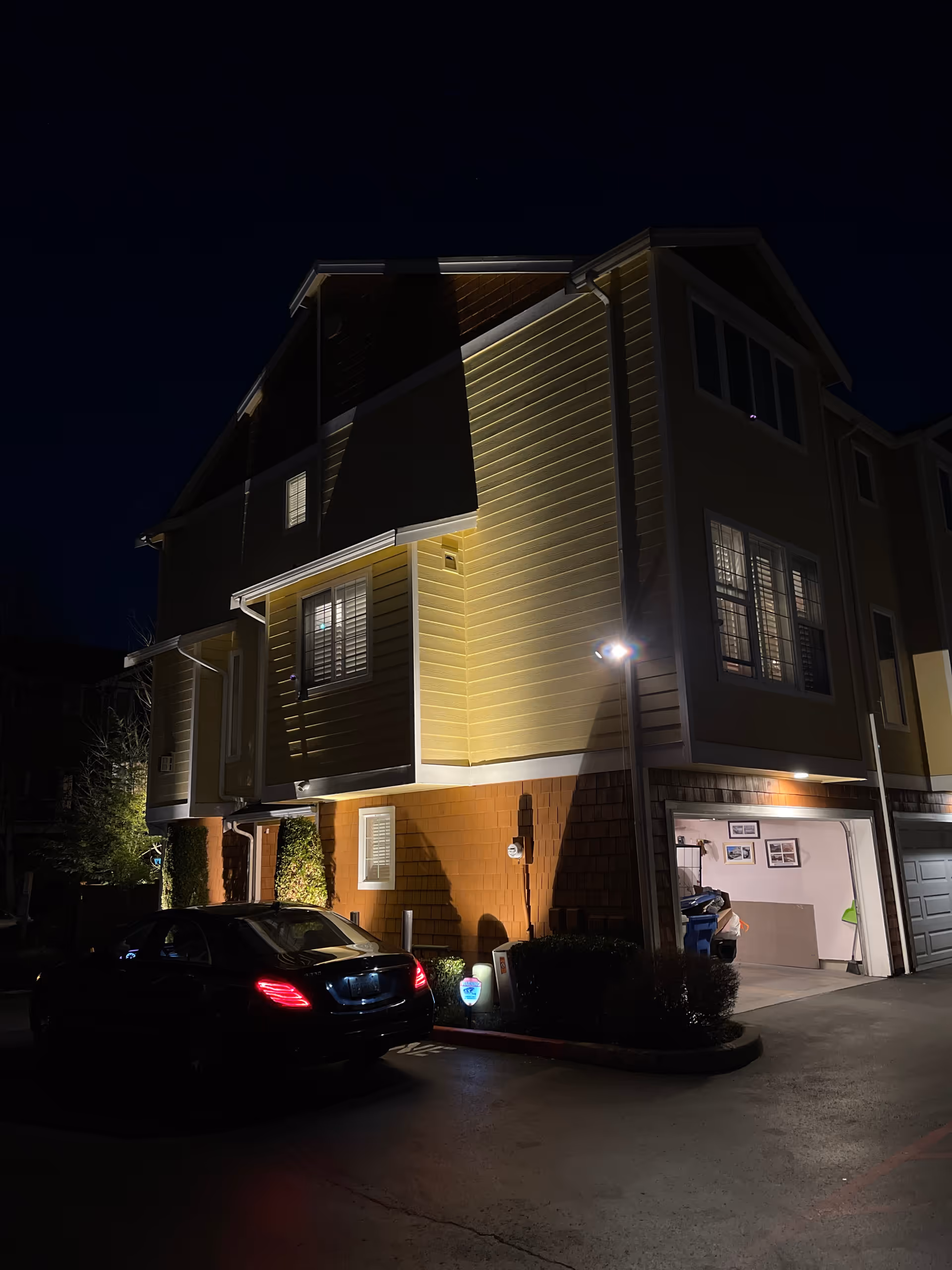 Nighttime exterior view of a multi-story senior living building with a lit garage and parked car.