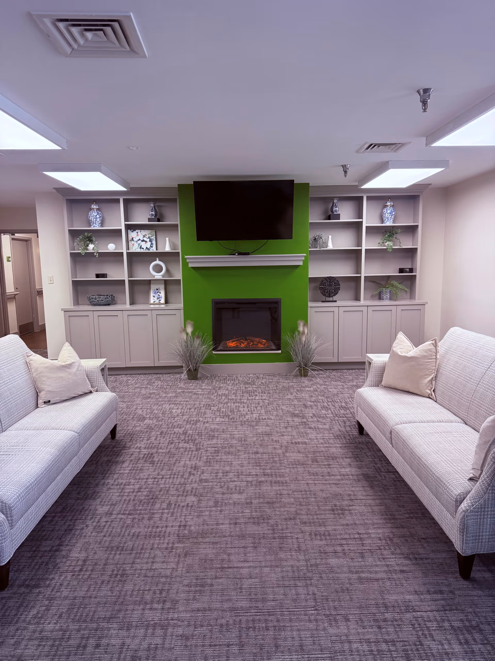 A comfortable resident lounge with two gray sofas, a green fireplace wall, and built-in shelves.