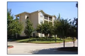 Exterior view of a beige multi-story senior living building with trees and a driveway.