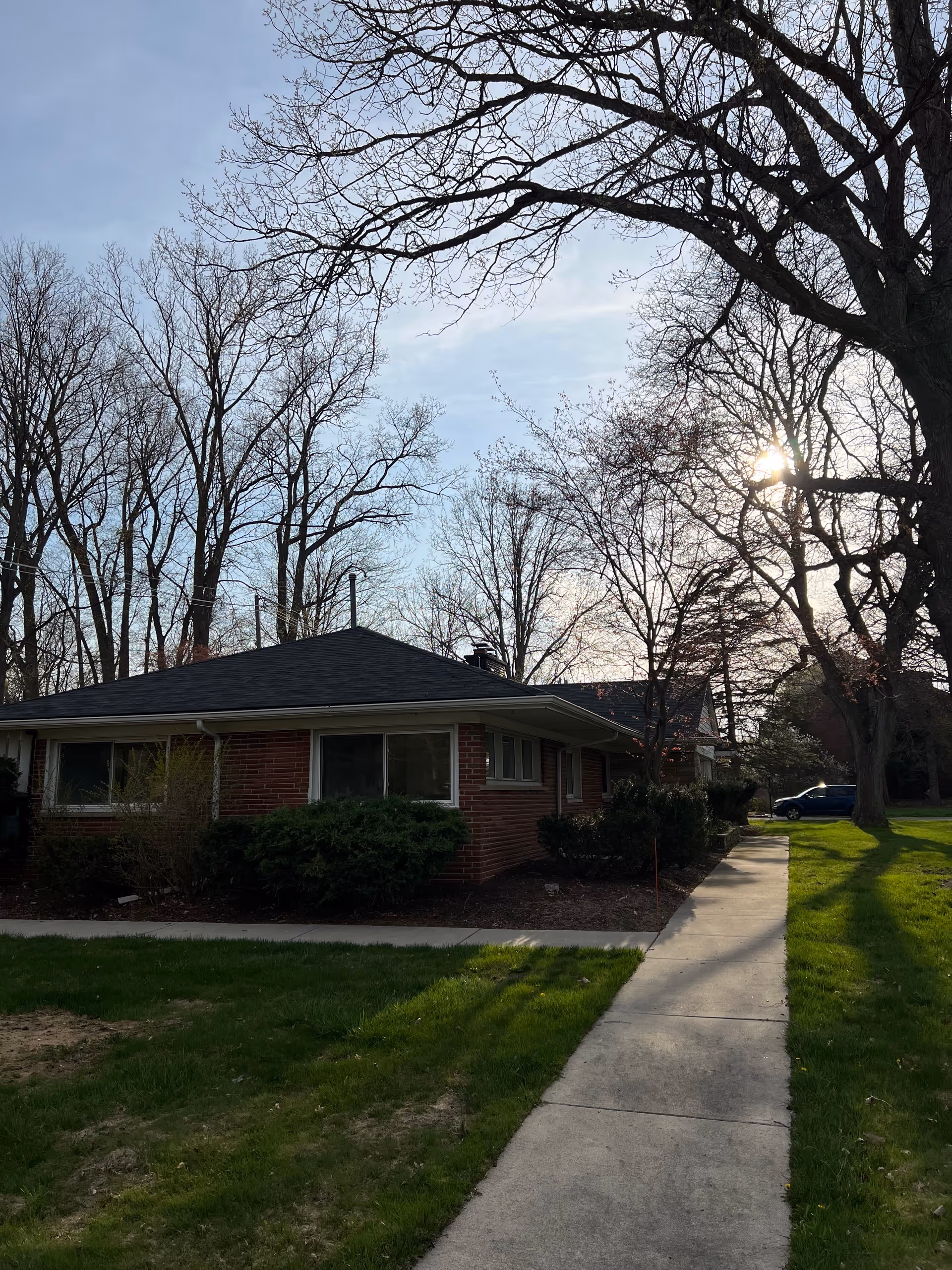 Single-story brick building with a sidewalk, trees, and well-kept lawn in a sunny setting.